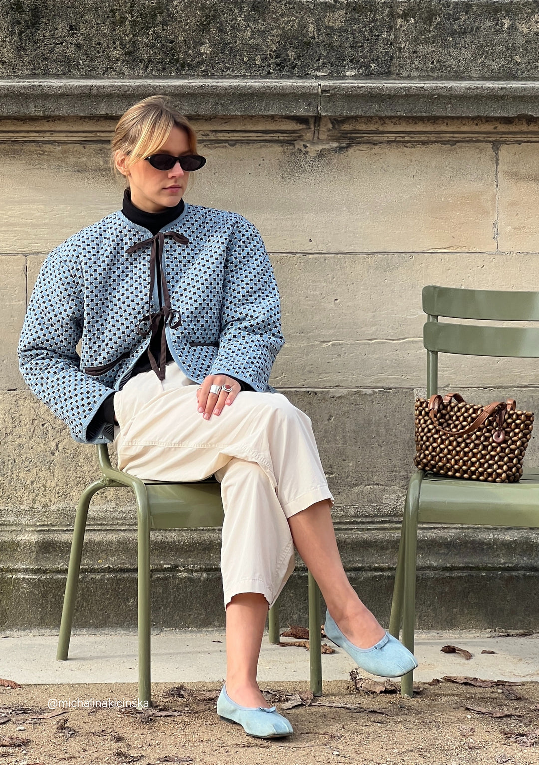 Person wearing TBCo Quilted Cotton Jacket in Reversible Blue Celestial Stripe, styled with white trousers and blue flats on green chair