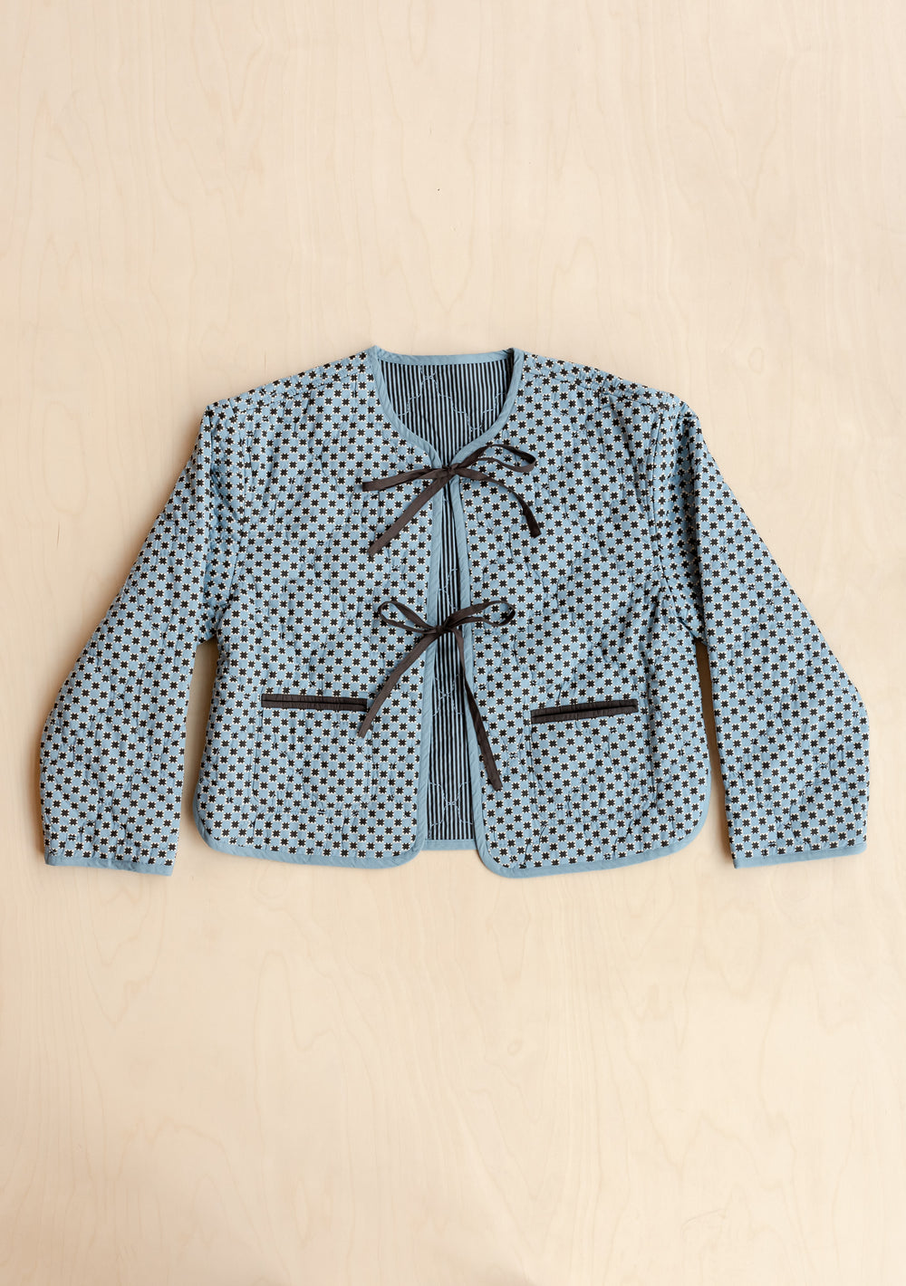 TBCo reversible quilted cotton jacket in blue celestial stripe with bow fastenings and patterned exterior, laid flat