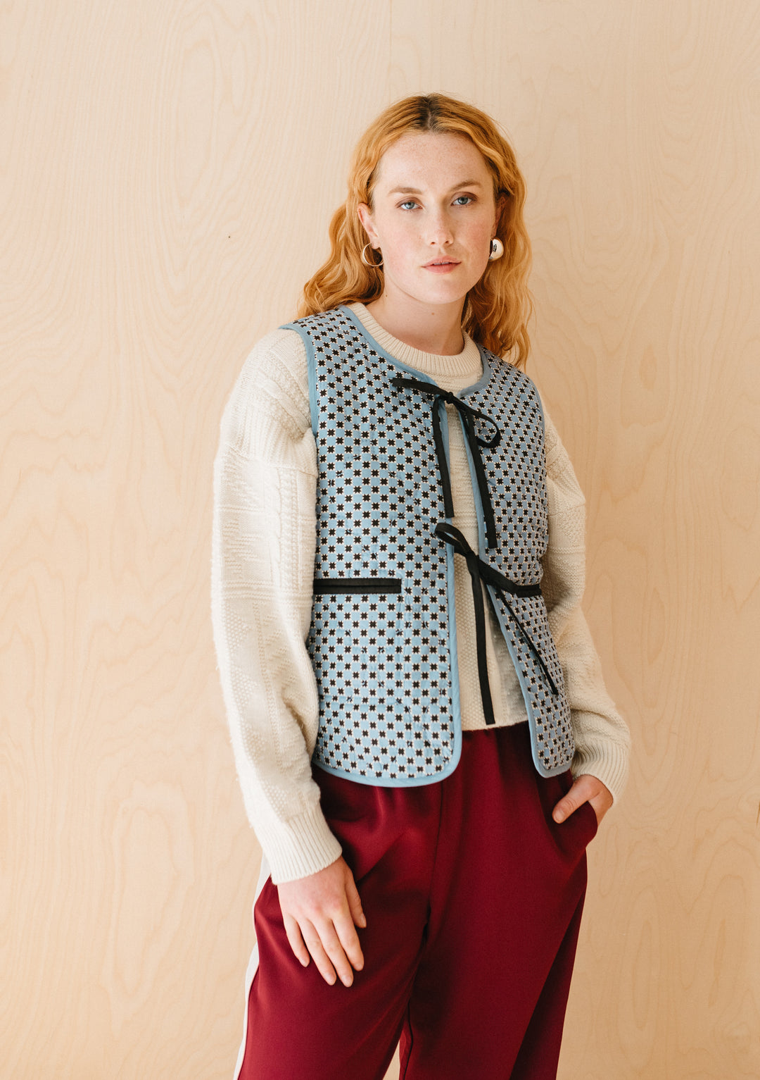 TBCo Quilted Cotton Vest in Reversible Blue Celestial Stripe with bow fastenings, styled with cream jumper and burgundy trousers