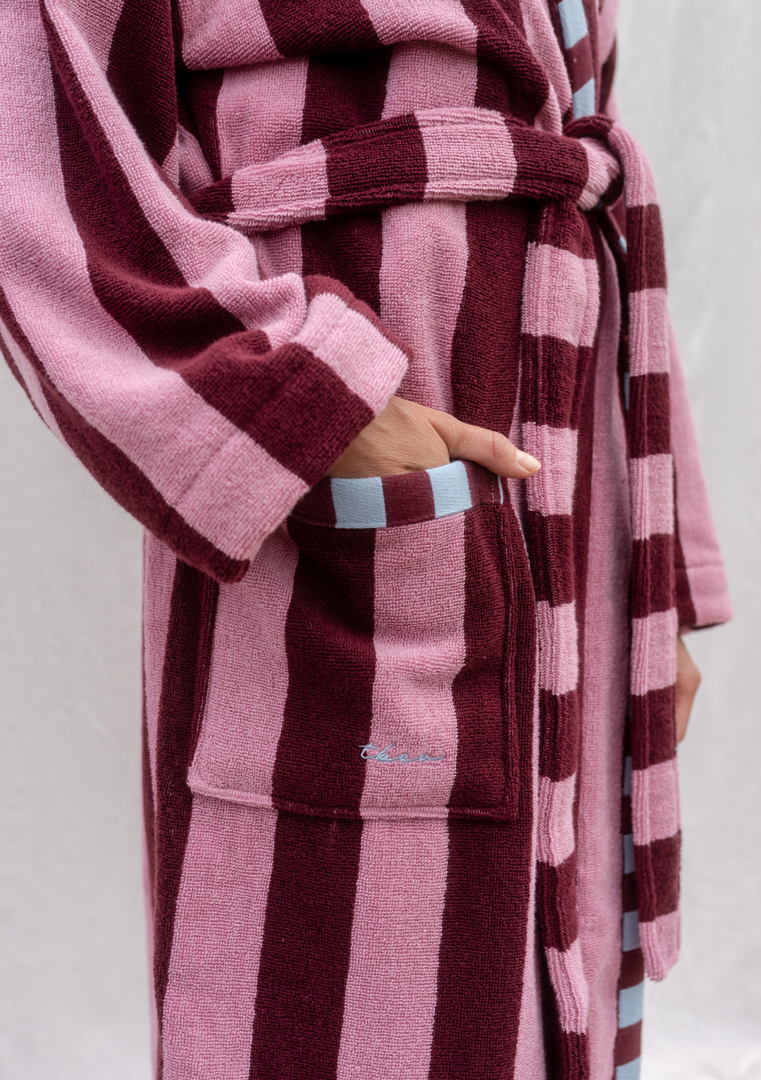 Close-up of TBCo Cotton Bath Robe in Burgundy Stripe with contrasting trim and hand in pocket.