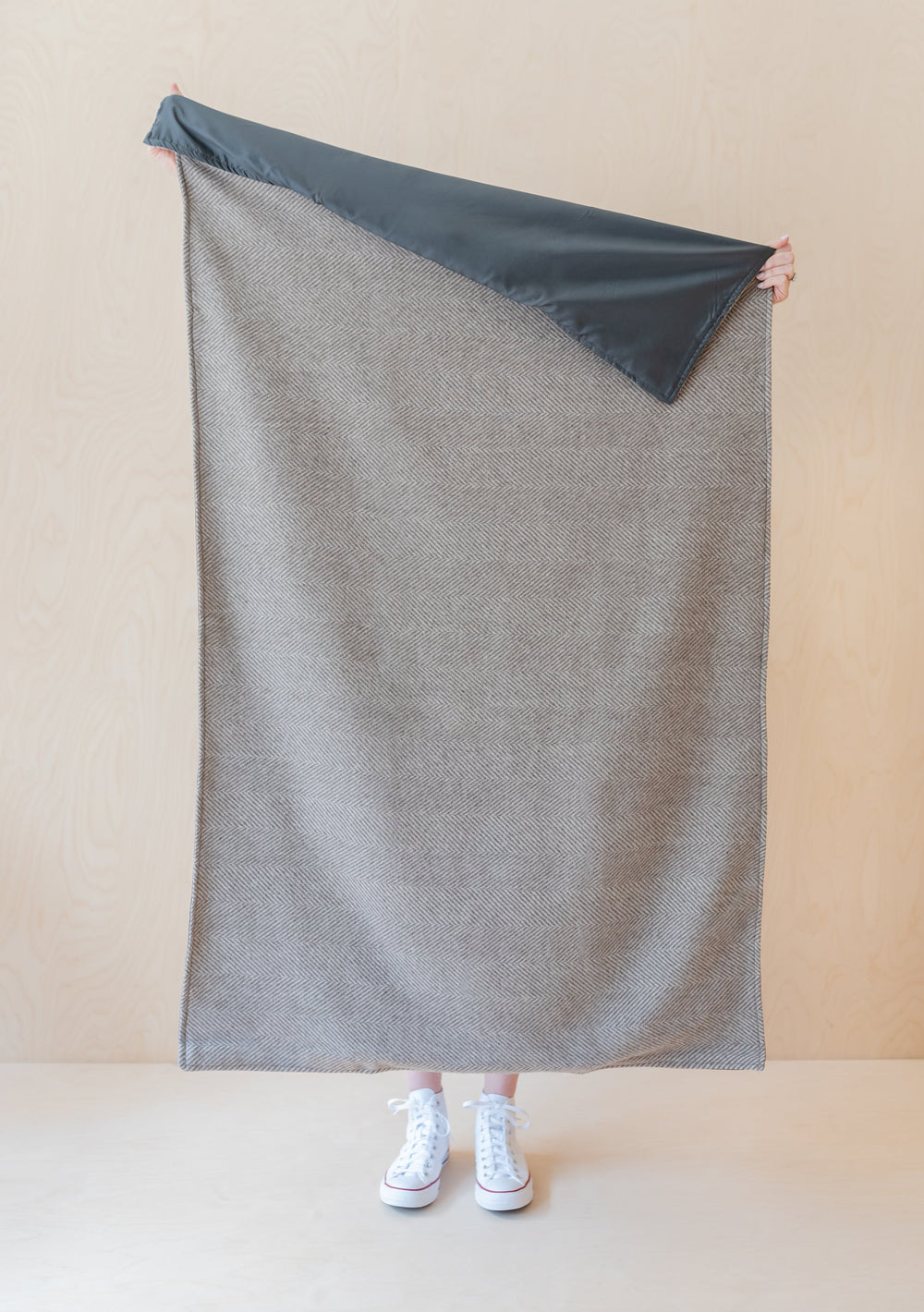 TBCo Recycled Wool Small Picnic Blanket in natural herringbone pattern with water-resistant backing, shown unfolded and held upright