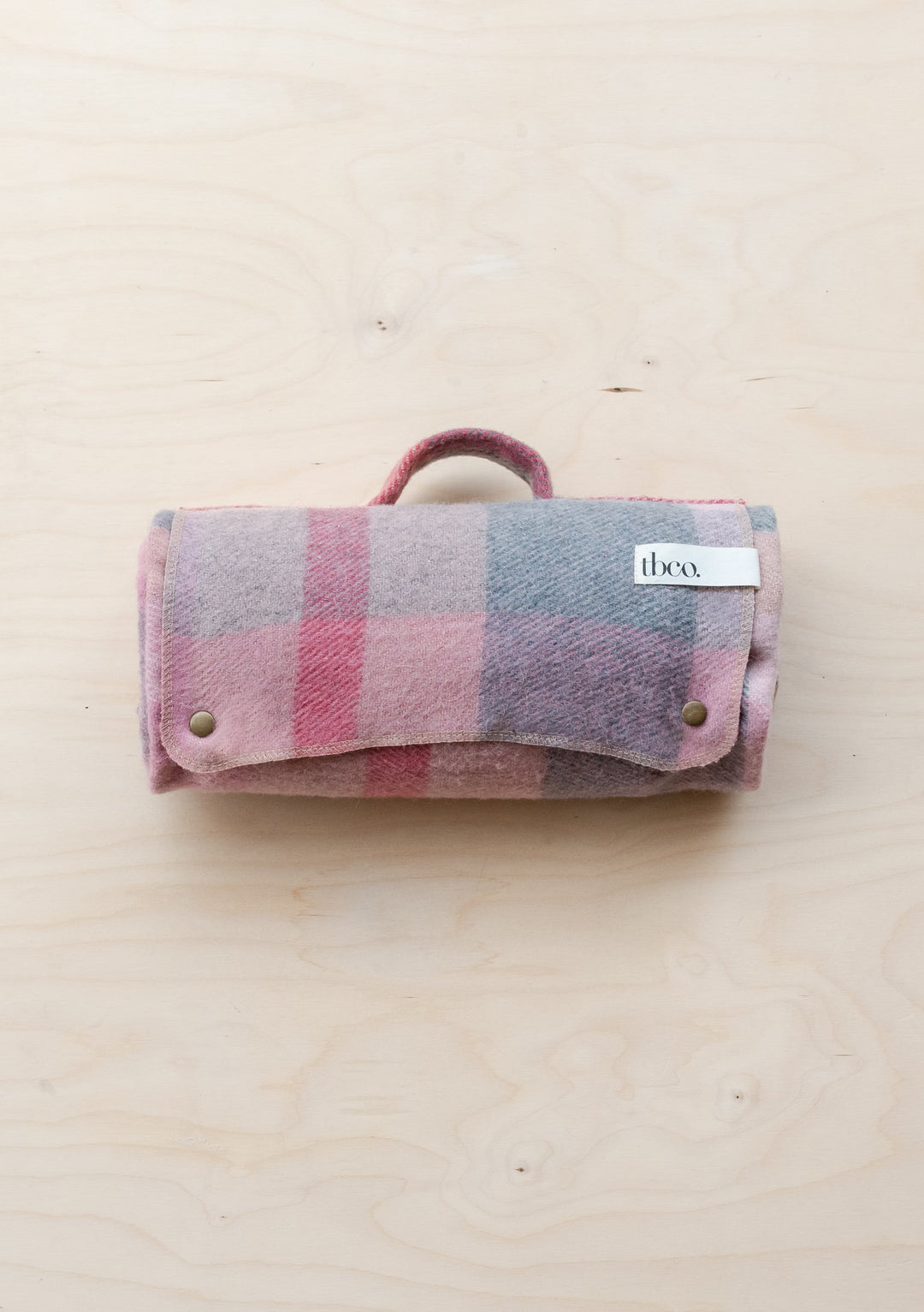 TBCo Recycled Wool Small Picnic Blanket in pink patchwork check pattern, rolled with carrying handle, displayed on wooden surface