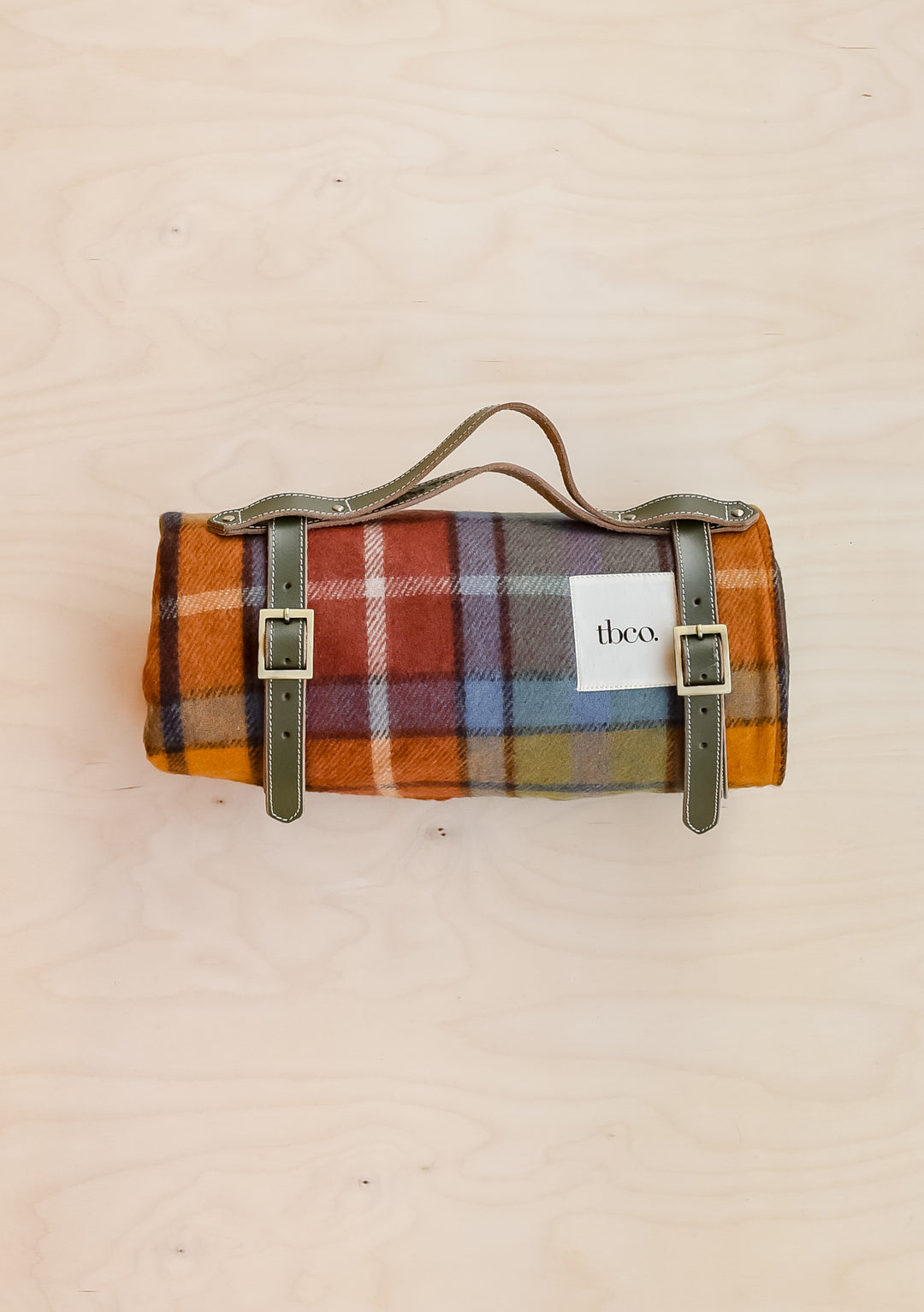 A TBCo recycled wool picnic blanket in Buchanan Antique Tartan, rolled up and held in a leather TBCo picnic carrier.