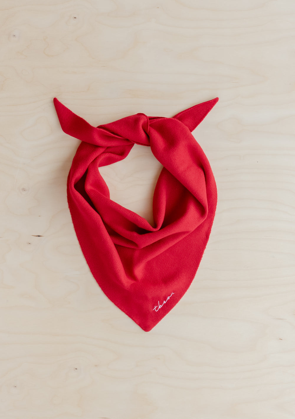 Red merino wool TBCo triangle scarf styled in classic bandana knot on light wooden surface