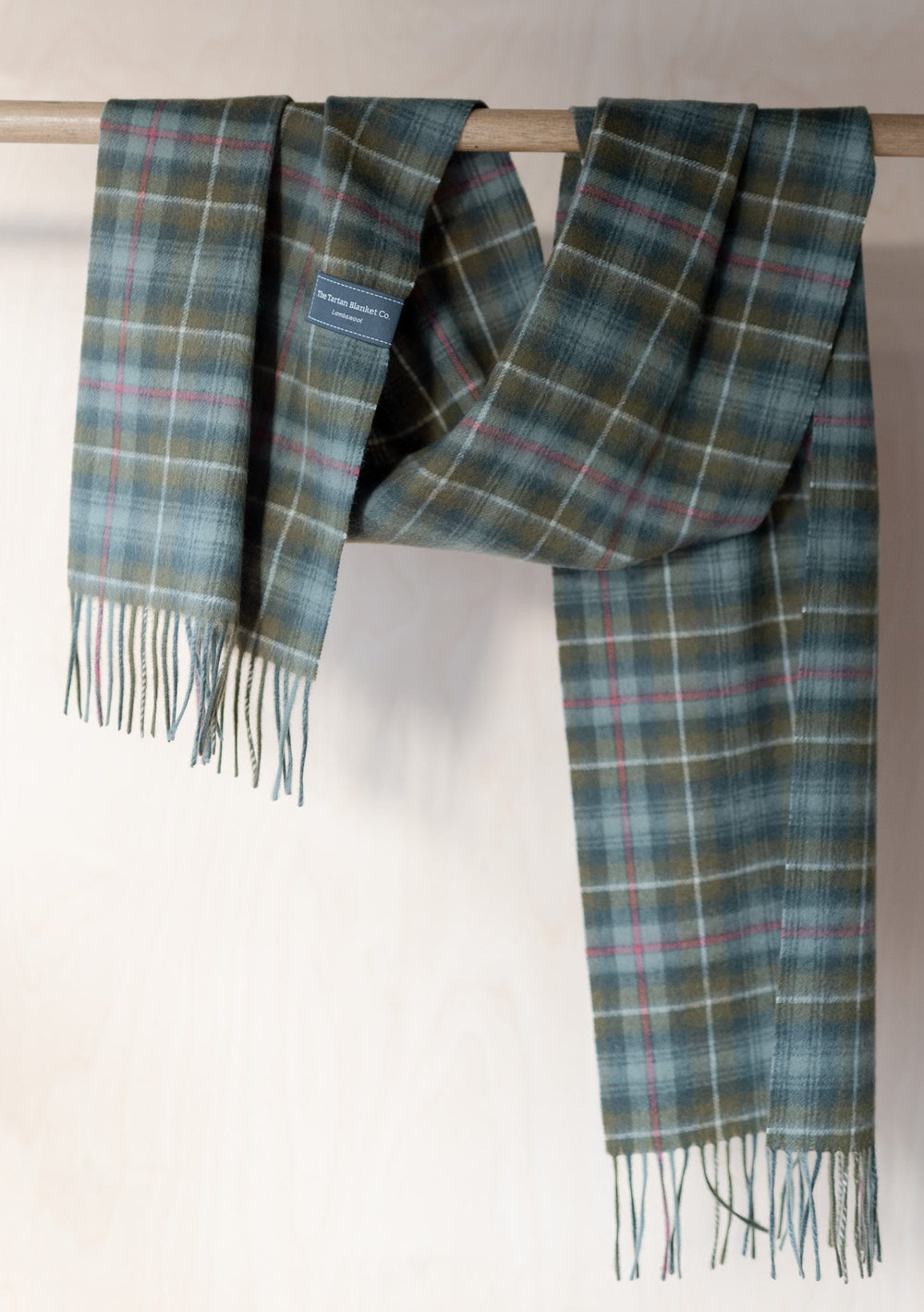 TBCo Mens Lambswool Scarf in Mackenzie Weathered Tartan displayed draped over wooden rail showing plaid pattern and fringed ends