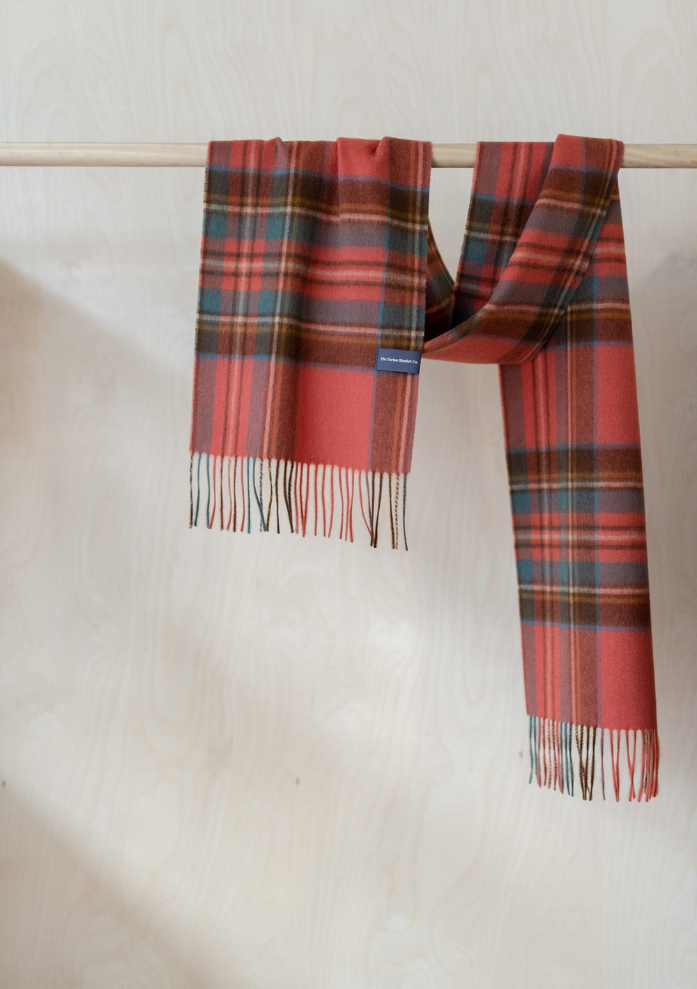 TBCo Men's Lambswool Scarf in Stewart Royal Antique Tartan hanging on wooden rail, displaying fringed ends and classic plaid pattern