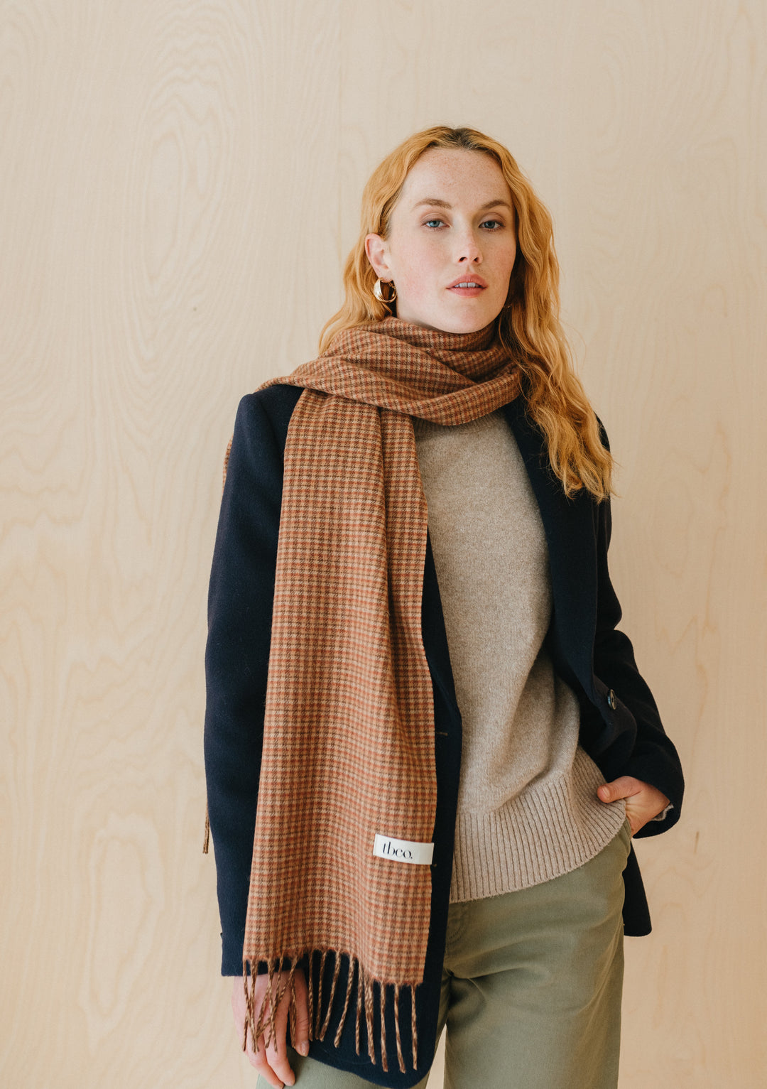 TBCo Lambswool Scarf in Camel Tweed Check elegantly draped over navy coat, showcasing brown and rust check pattern with fringe detail