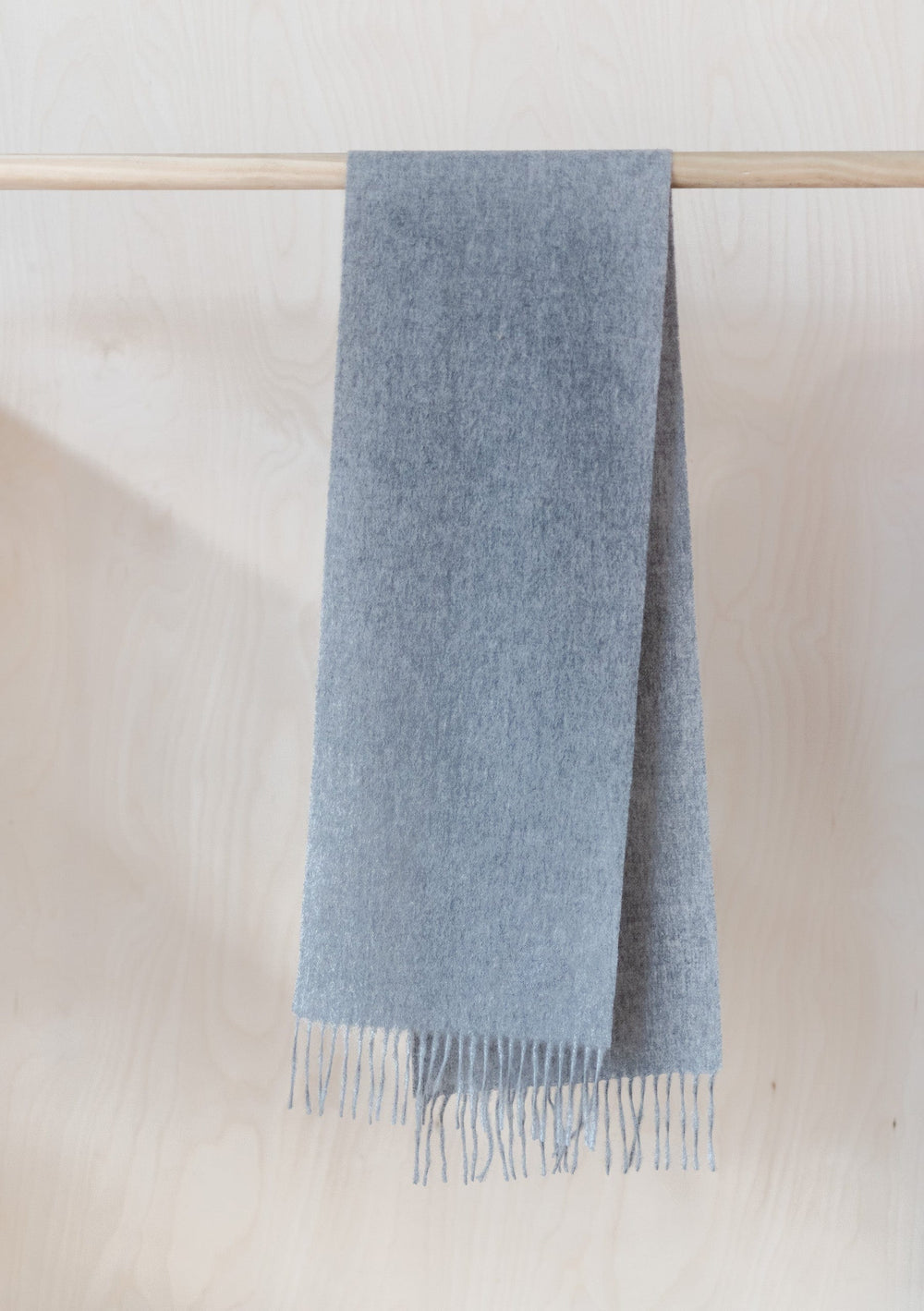 TBCo Kids Lambswool Scarf in Grey Melange hanging on wooden rail, showing soft texture and fringed edge details