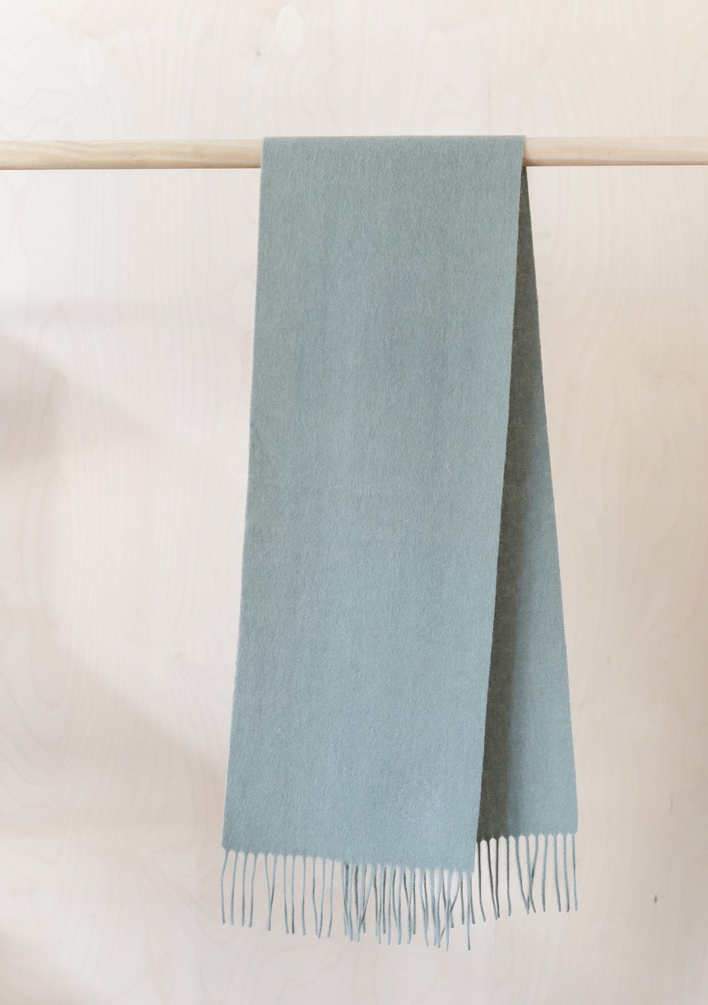 TBCo Kids Lambswool Scarf in Sage Melange hanging on wooden rail, showing soft texture and fringed detail