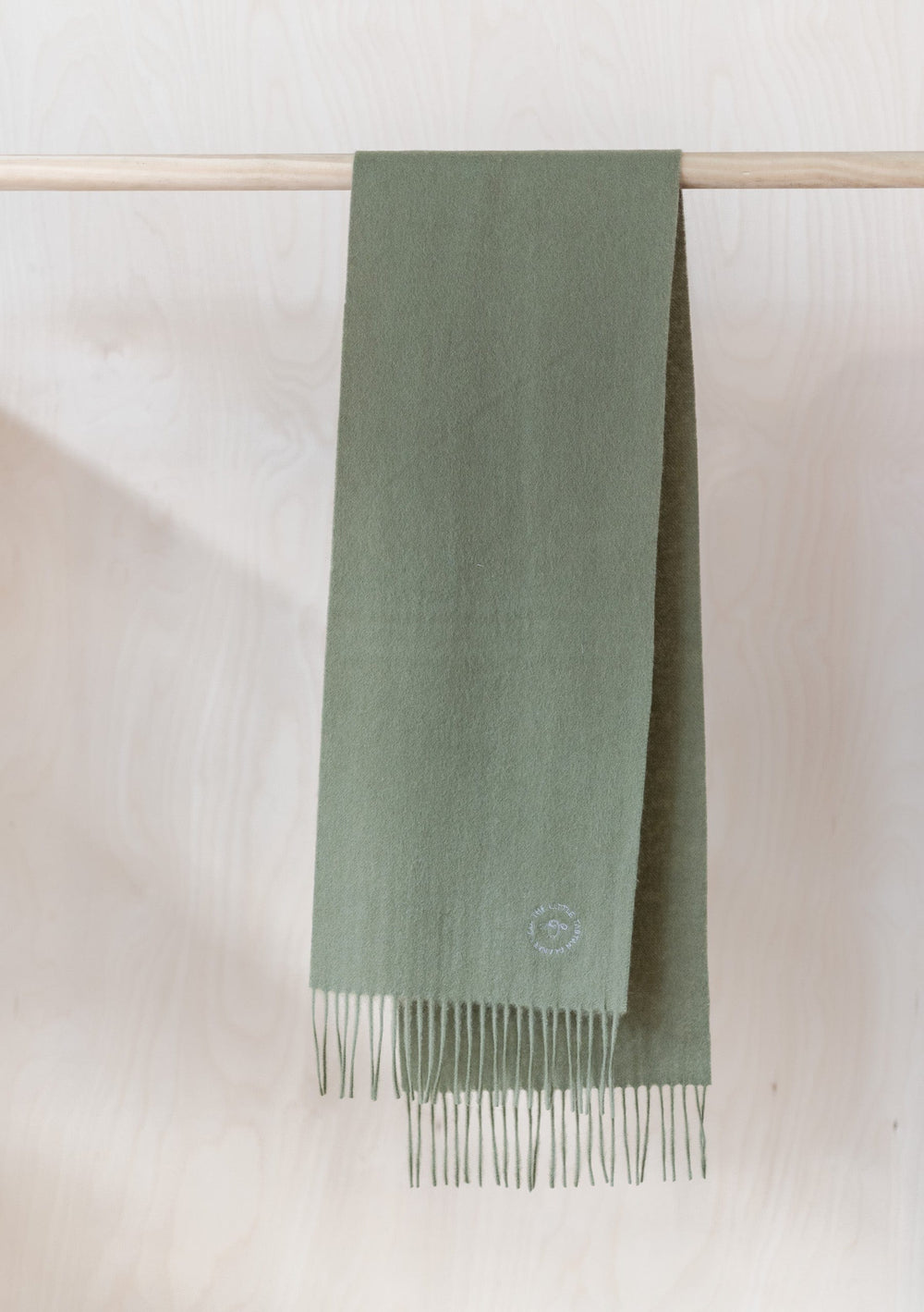 TBCo Lambswool Kids Scarf in Olive hanging on wooden rail, displaying soft texture and fringed ends