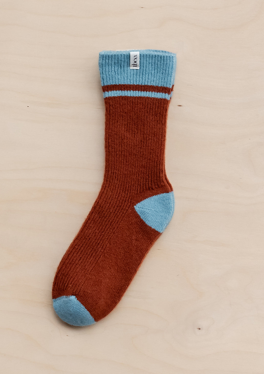 TBCo Merino Striped Socks in rust colour with light blue accents on cuff, heel and toe, displayed on wooden background