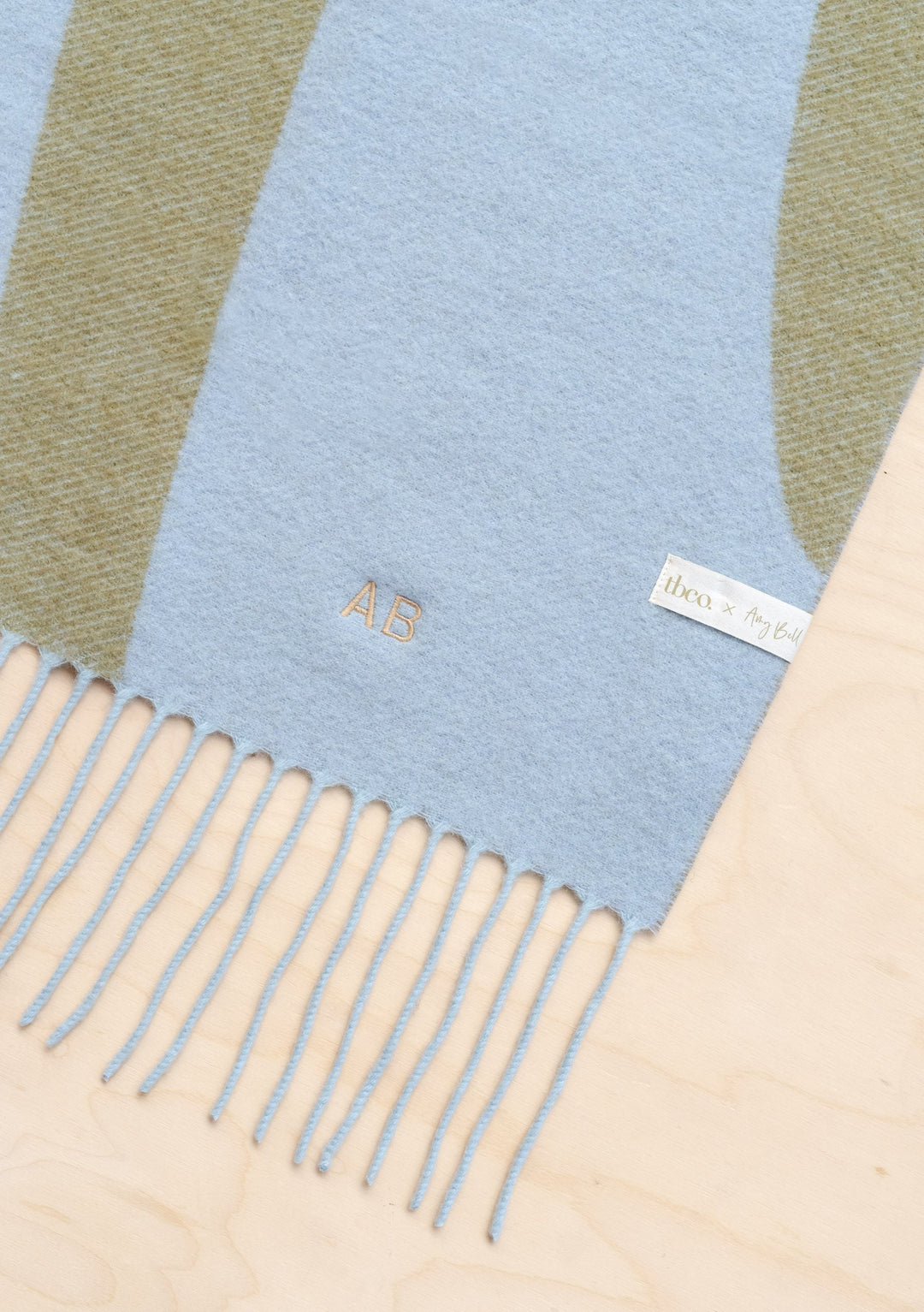 TBCo x Amy Bell Spencer 2.0 scarf in monochrome check pattern with light blue and beige stripes, featuring fringed edge