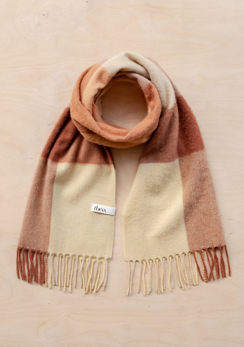 TBCo lambswool oversized scarf in buttermilk yellow and rust brown block check pattern with fringed ends, laid flat on beige surface