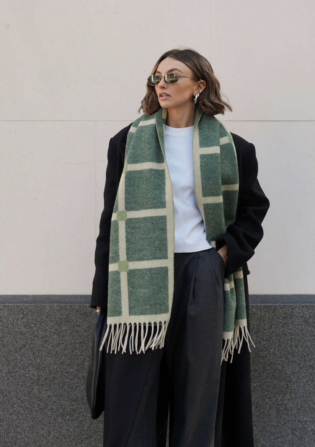 TBCo x Chloe Hayward Evergreen Reversible Scarf styled with black winter coat, featuring green and cream grid check pattern