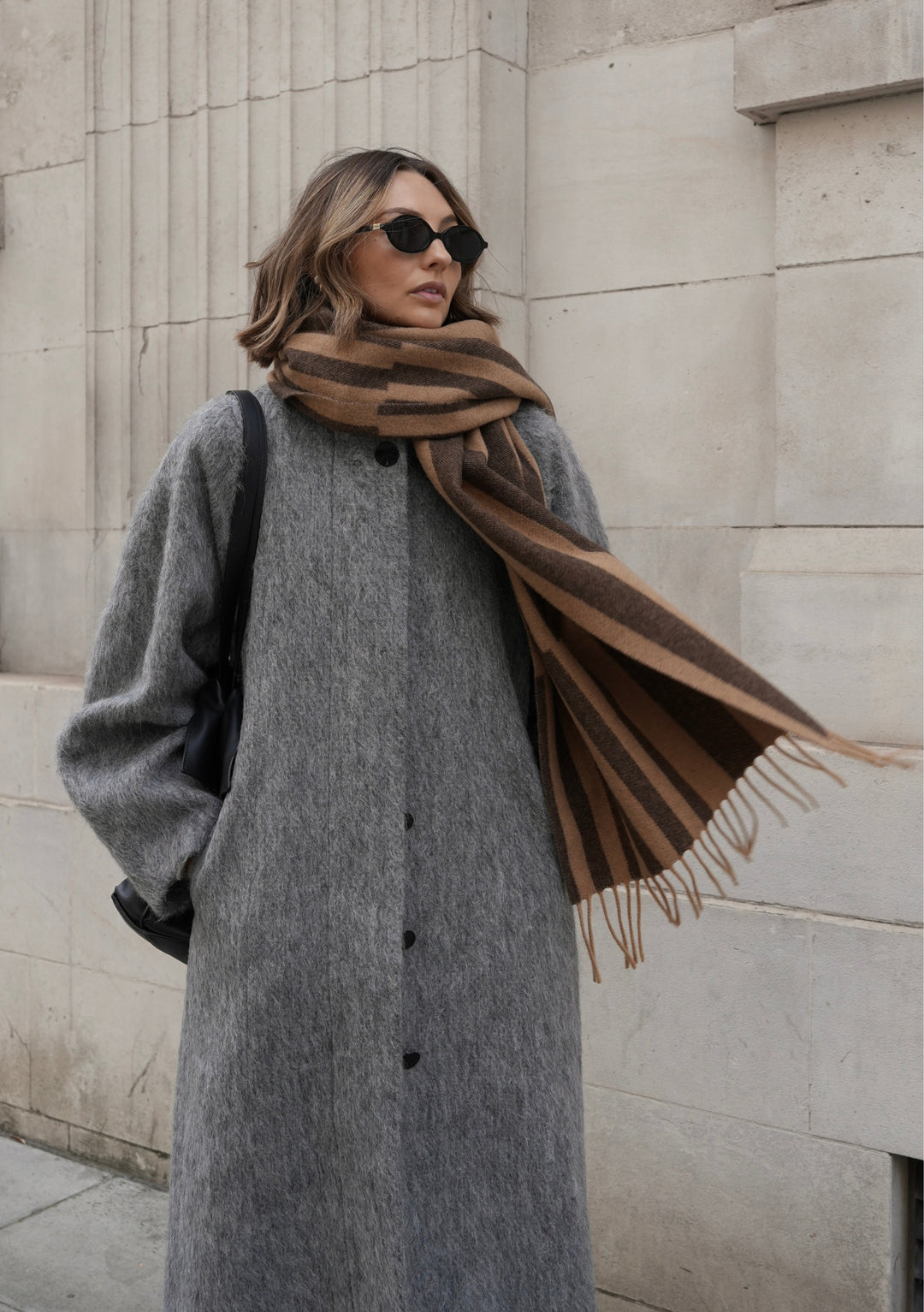 Stylish person wearing TBCo x Chloe Hayward Espresso Stripe lambswool scarf with grey coat against stone architecture