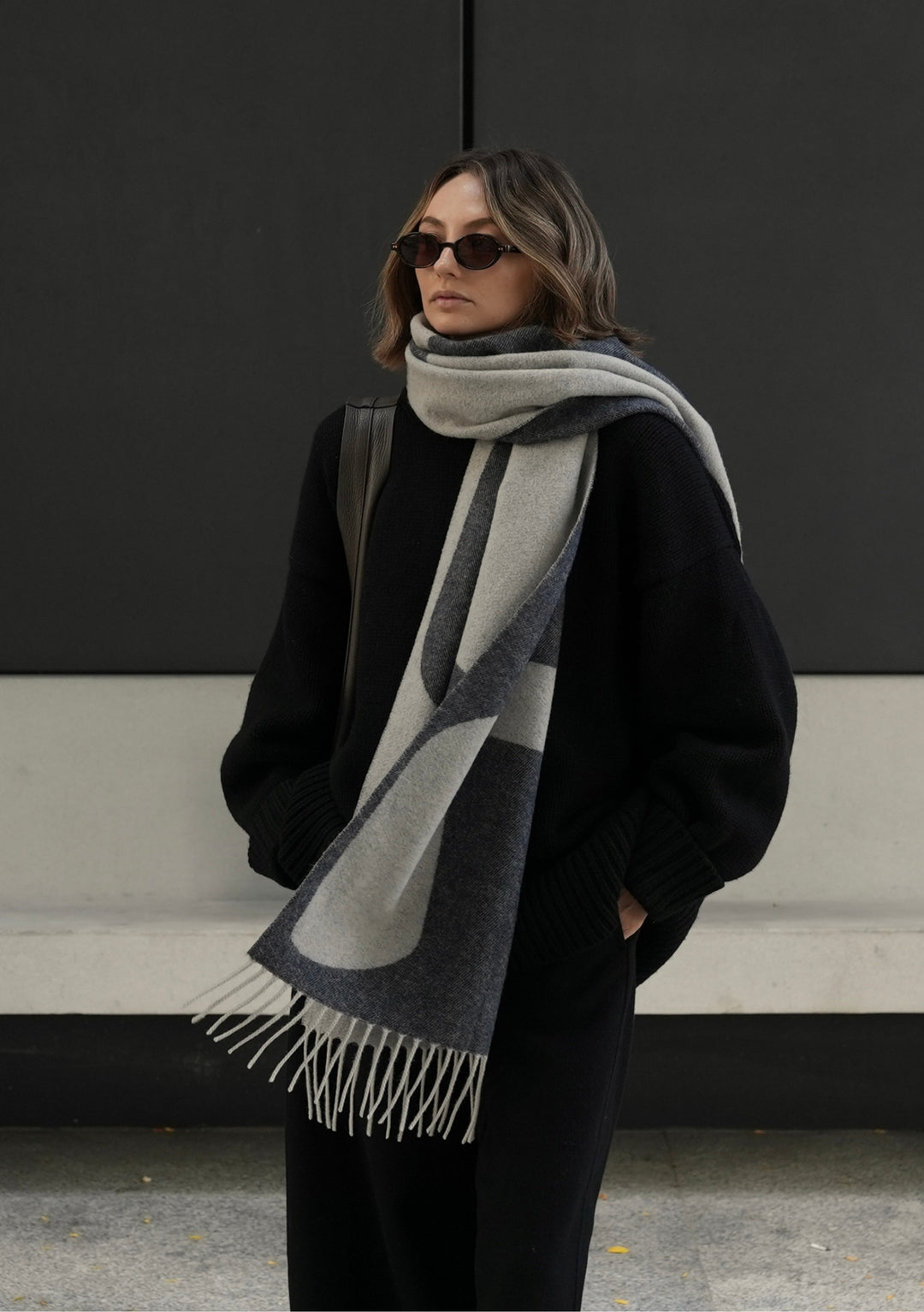 A person wearing TBCo x Chloe Hayward Silver Lining Reversible lambswool scarf in grey and cream with minimalist abstract pattern