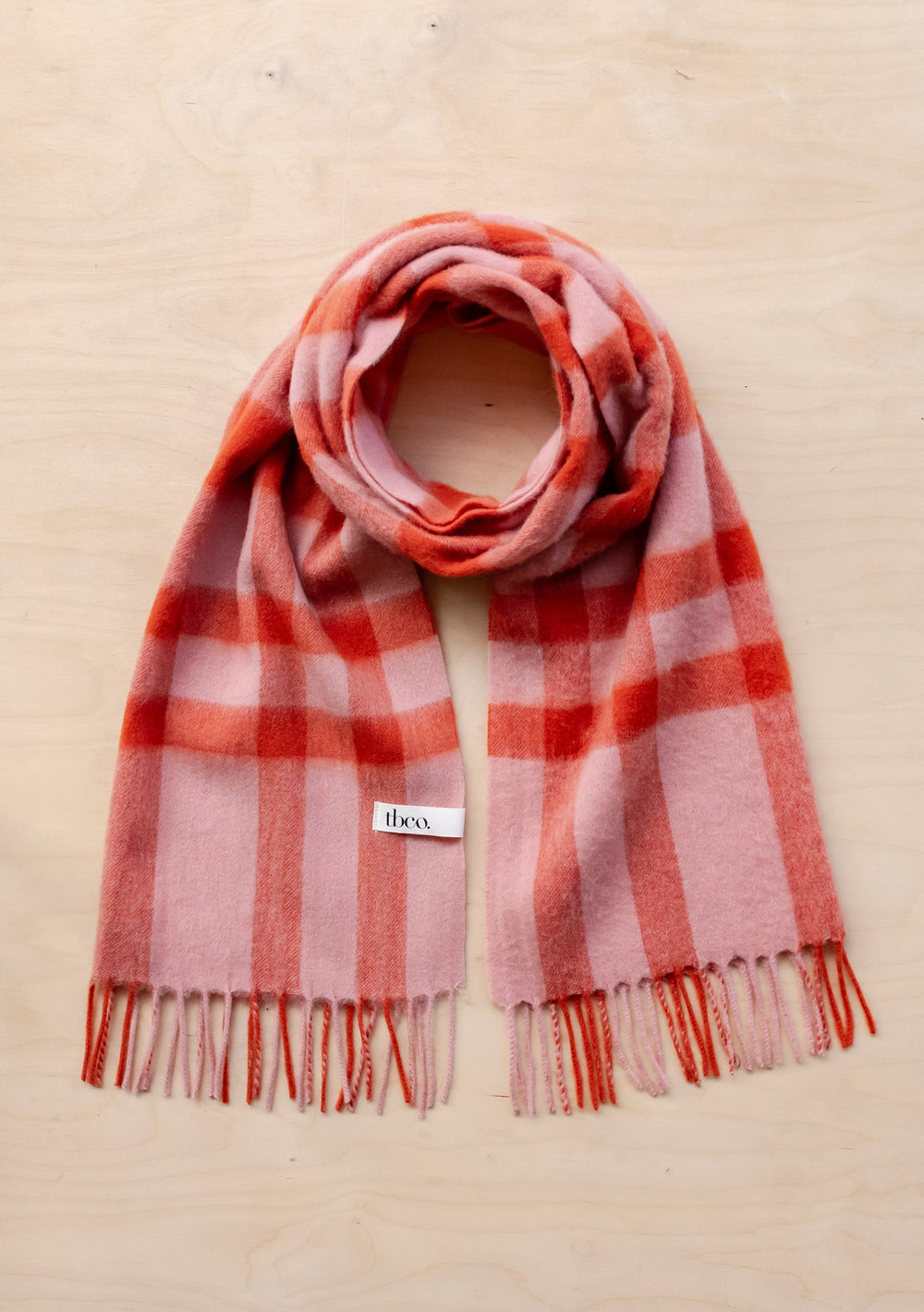 TBCo lambswool oversized scarf in pink and red check pattern with fringe detail, displayed flat on cream background