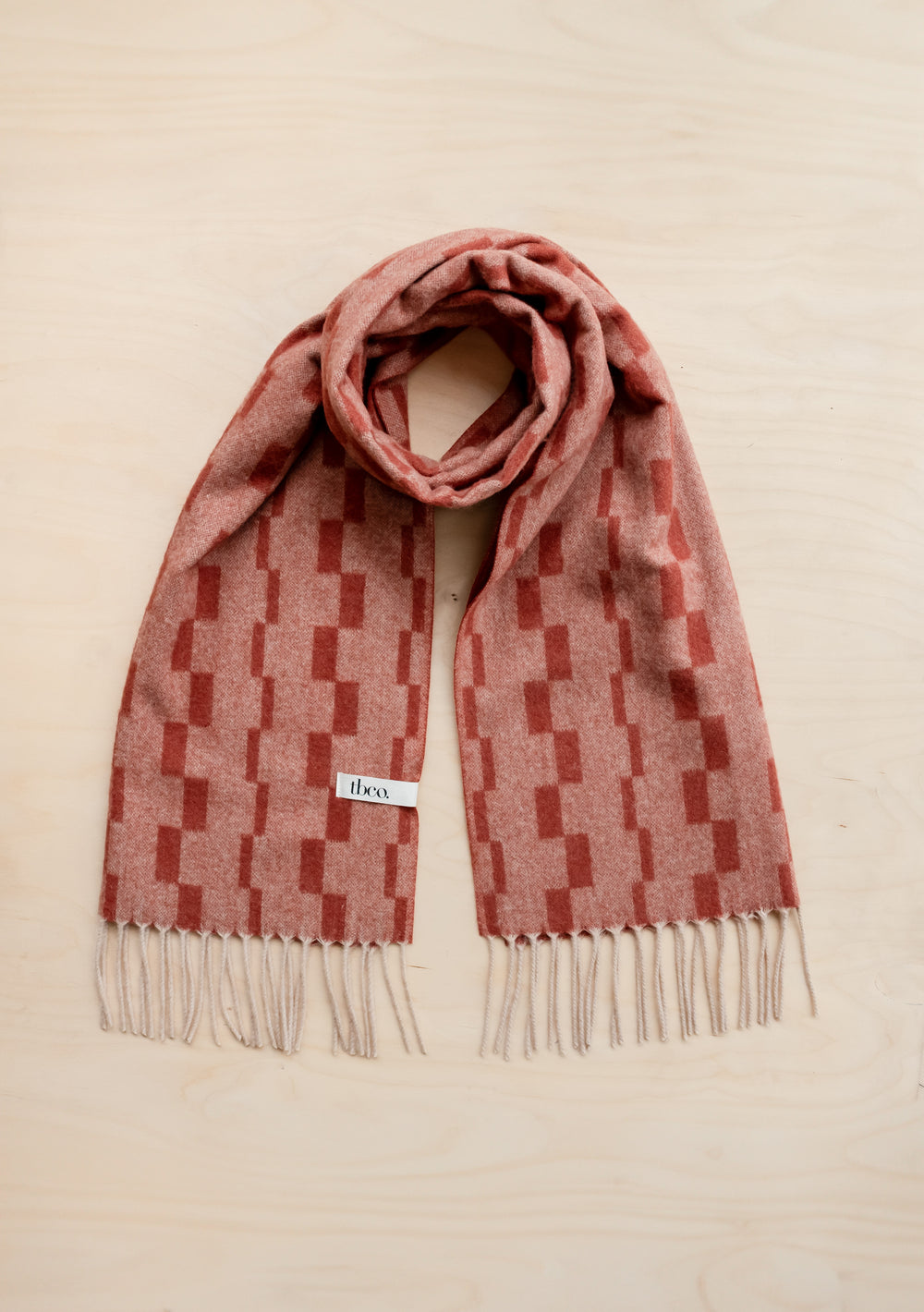 TBCo Lambswool Oversized Scarf in Neutral Checker featuring rust and red stacked pattern with white fringe, laid flat on beige surface