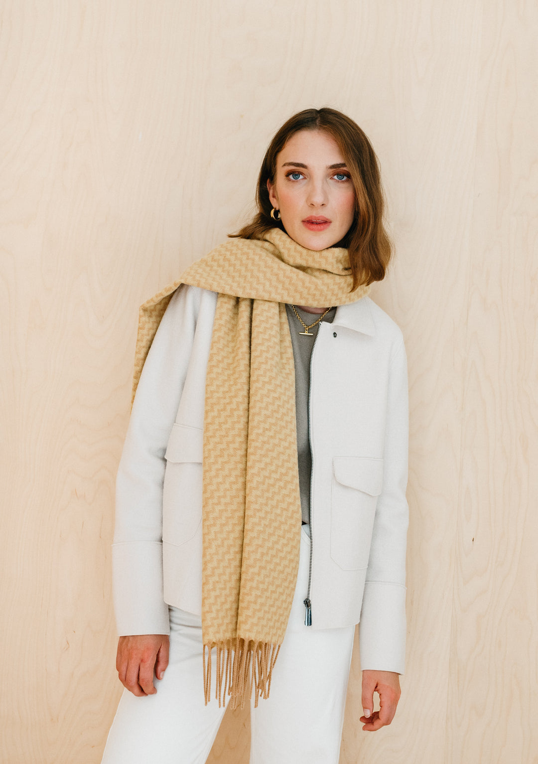 TBCo Lambswool Oversized Scarf in Buttermilk Chevron styled with white winter coat, showing camel and cream zigzag pattern and fringe detail