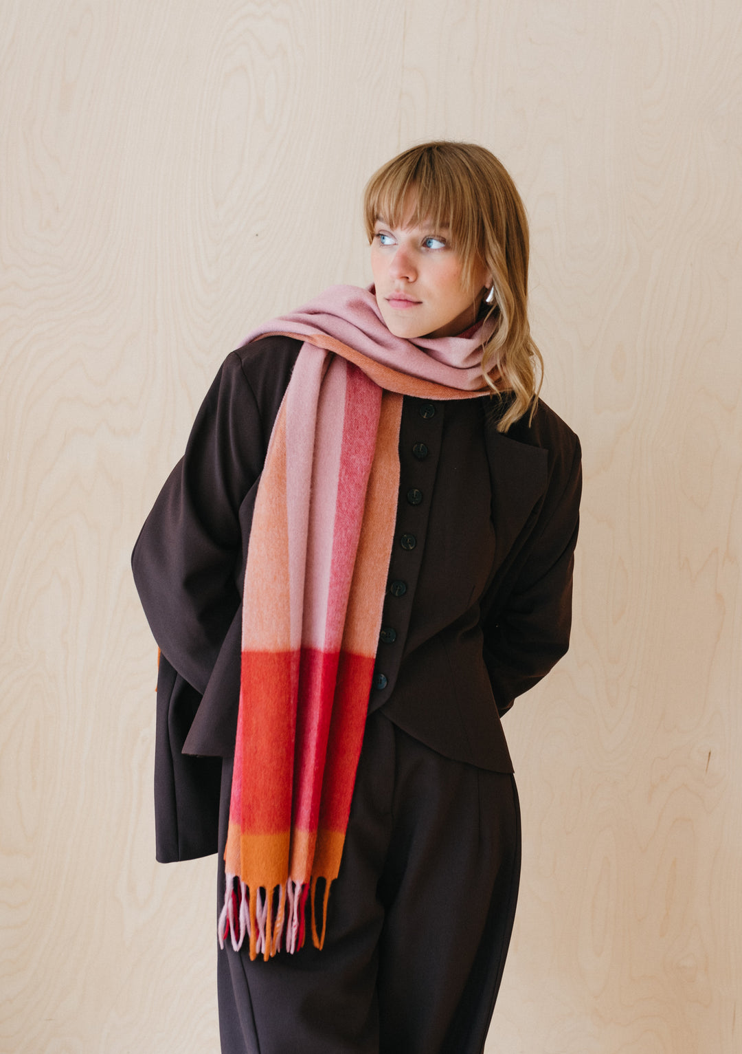 TBCo Berry Edge Check Lambswool Scarf styled with black coat, featuring pink, red and orange checked pattern with fringed ends