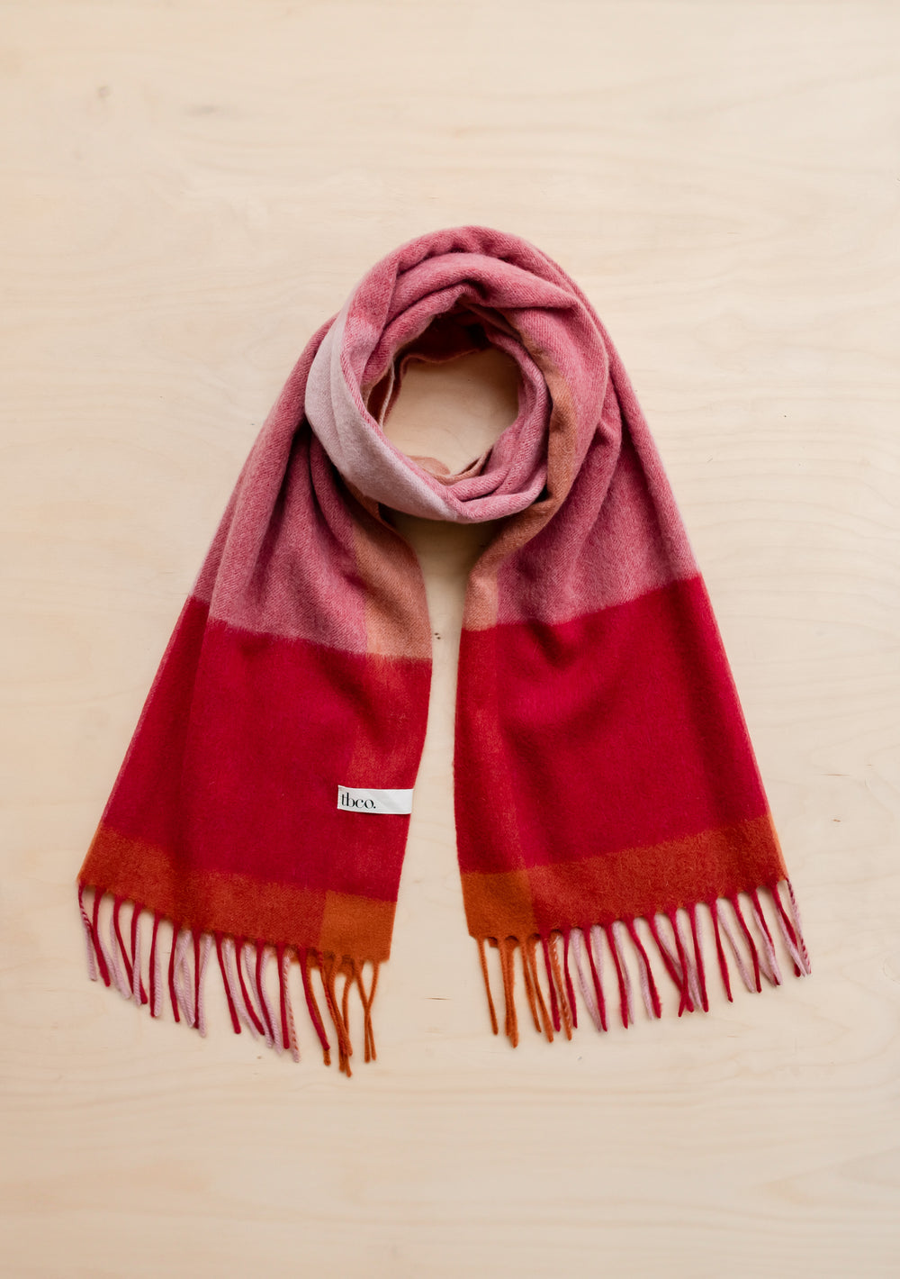 TBCo Lambswool Oversized Scarf in Berry Edge Check features pink, red and orange colour blocks with fringed ends laid flat