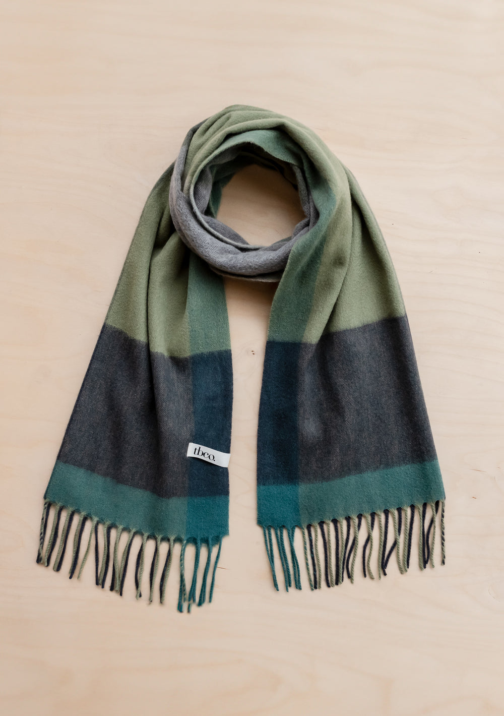 TBCo Lambswool Oversized Scarf in Green Edge Check displayed flat showing forest green, sage and charcoal check pattern with fringe