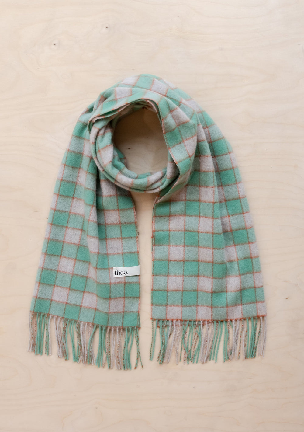 TBCo Lambswool Oversized Scarf in mint green and grey gingham pattern with fringed ends, displayed flat on beige surface