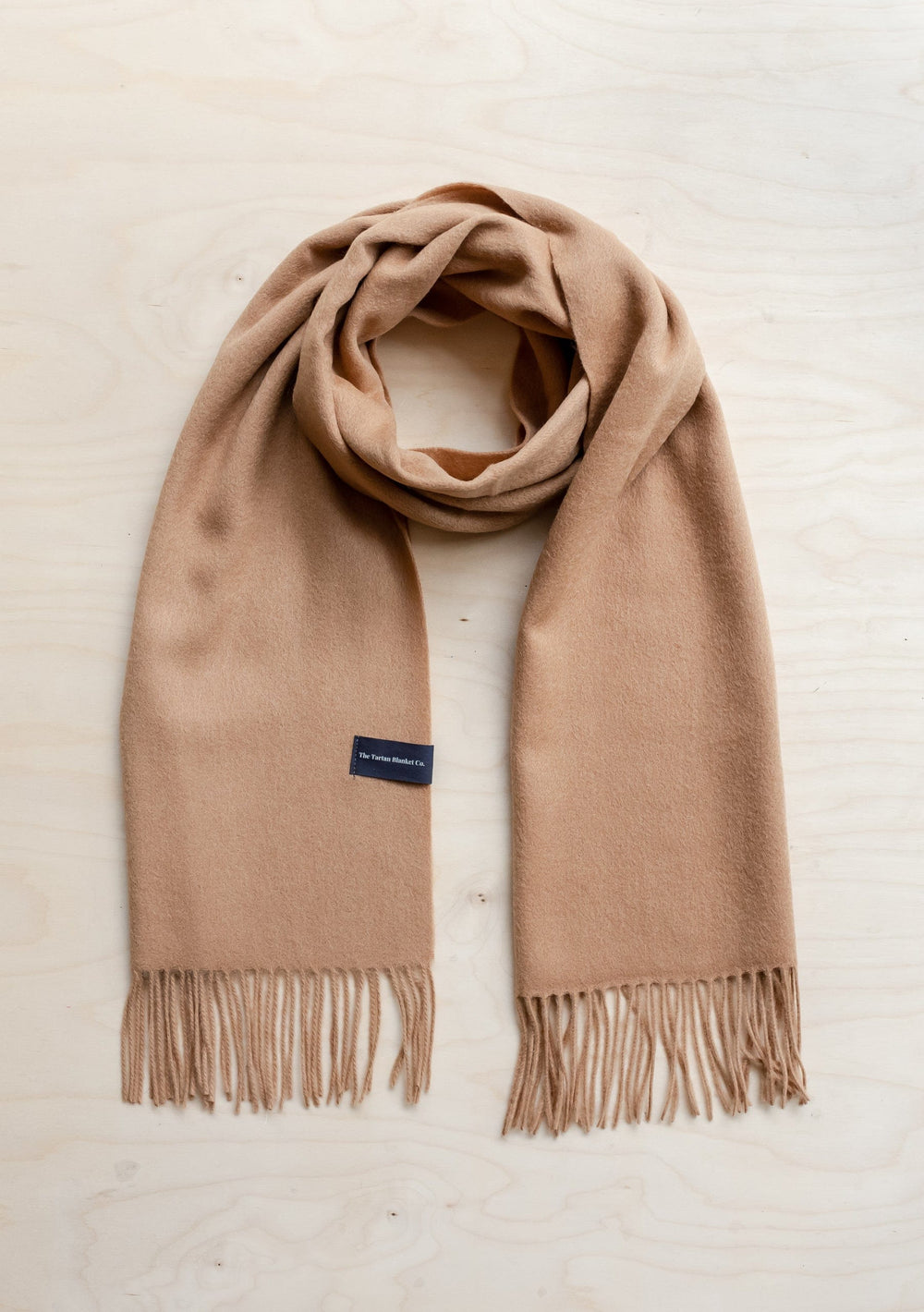 Soft camel-coloured TBCo lambswool oversized scarf with fringe detail, displayed flat against white background