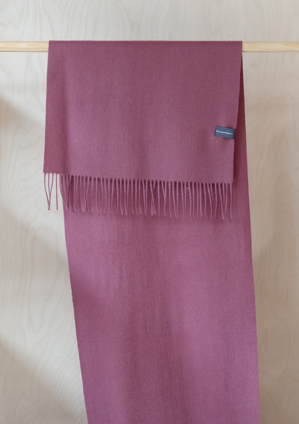 TBCo Lambswool Oversized Scarf in Mulberry displayed draped on wooden hanger, showing fringed detail and rich mulberry colour