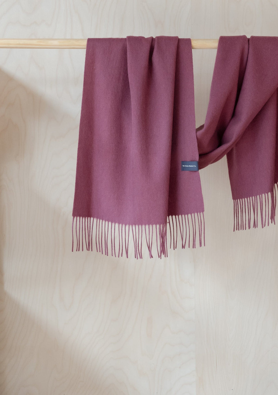 TBCo mulberry lambswool oversized scarf with fringe detail draped elegantly over wooden rail showing soft texture and length