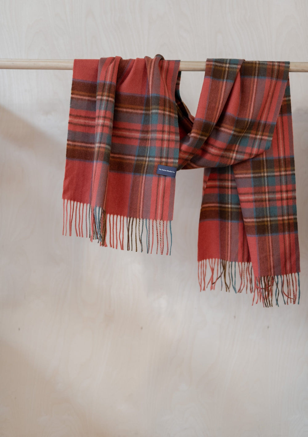 TBCo Lambswool Oversized Scarf in Stewart Royal Antique Tartan draped on wooden rail showing fringe and plaid pattern