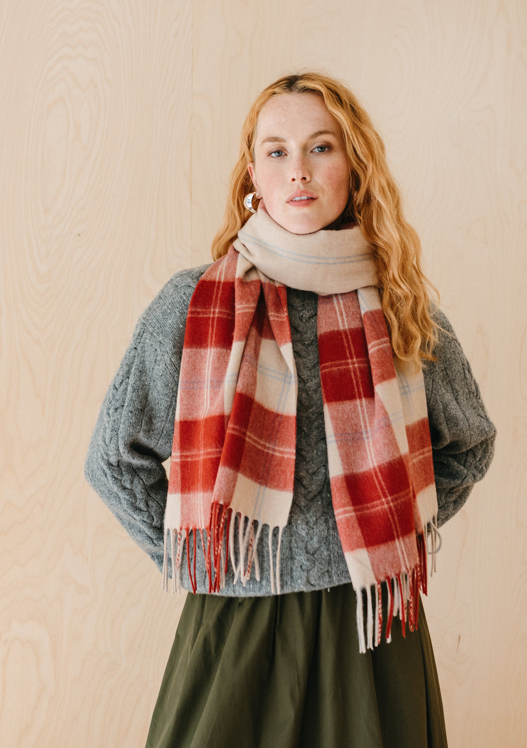 TBCo Lambswool Oversized Scarf in Red Varsity Check styled with grey cable knit jumper and olive skirt against wooden backdrop