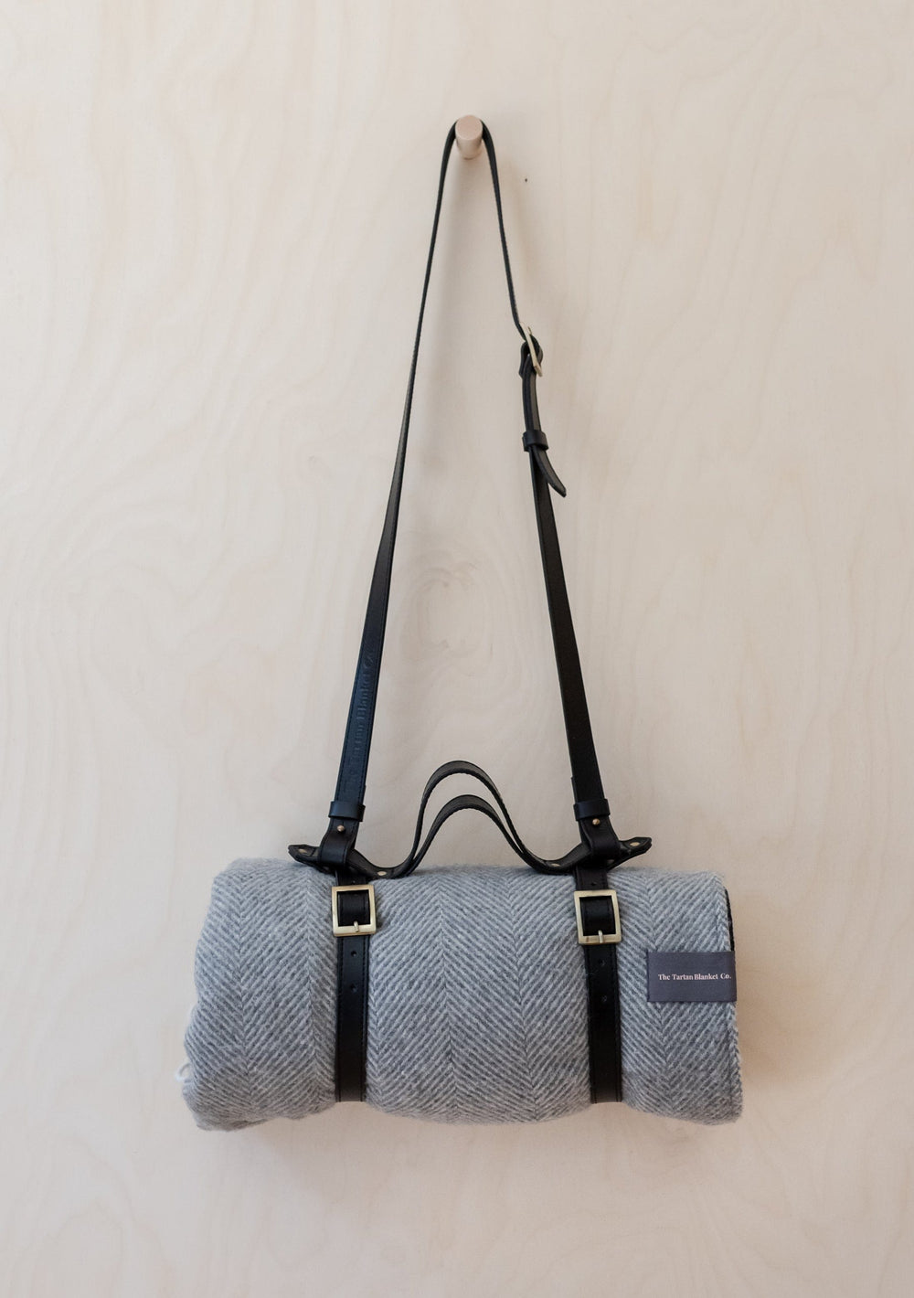 TBCo leather picnic carrier with adjustable shoulder strap shown with grey herringbone wool blanket and brass buckles