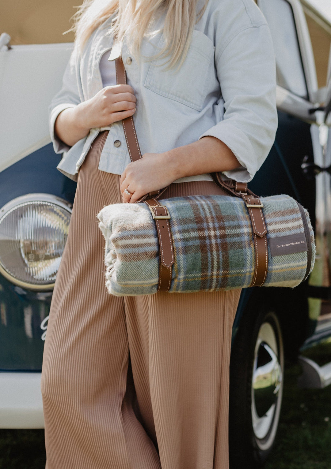 TBCo Leather Picnic Carrier with adjustable shoulder strap shown with plaid wool blanket, brown leather straps and brass hardware