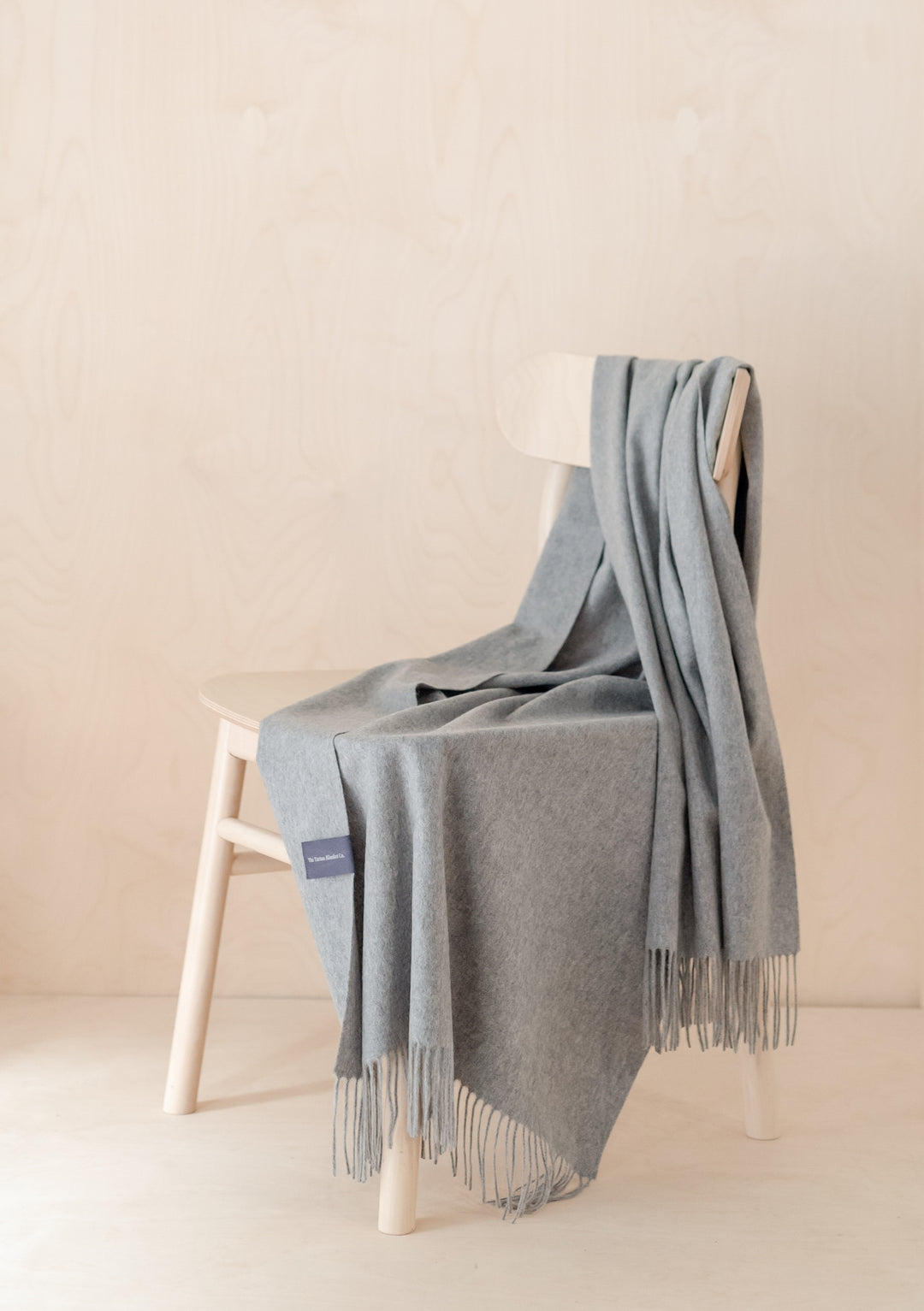 TBCo Cashmere Small Blanket in Light Grey Melange draped elegantly over white wooden chair, showcasing fringed edges