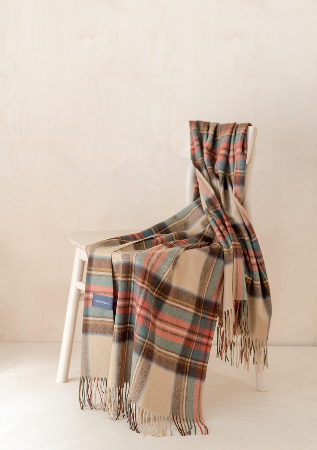 TBCo Cashmere Small Blanket in Stewart Dress Antique Tartan draped elegantly over white chair, showcasing fringed edges and plaid pattern