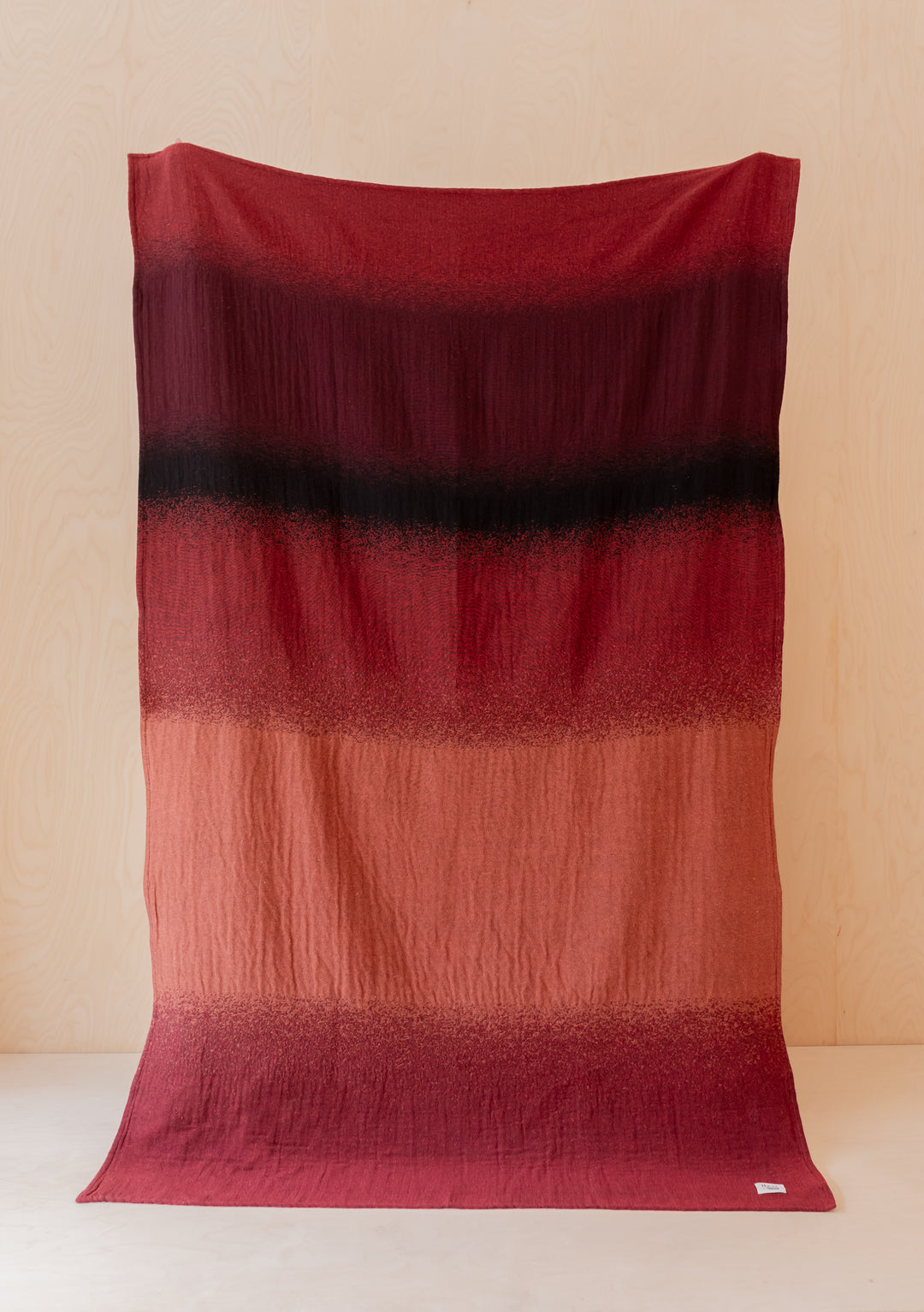 TBCo x Abisola Omole Hues Cotton Throw featuring gradient stripes in deep red, burgundy and charcoal tones against beige backdrop