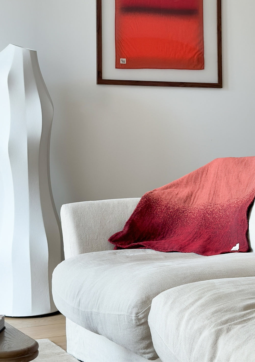 TBCo x Abisola Omole Hues Cotton Throw in gradient red and burgundy draped over white sofa, with matching artwork above