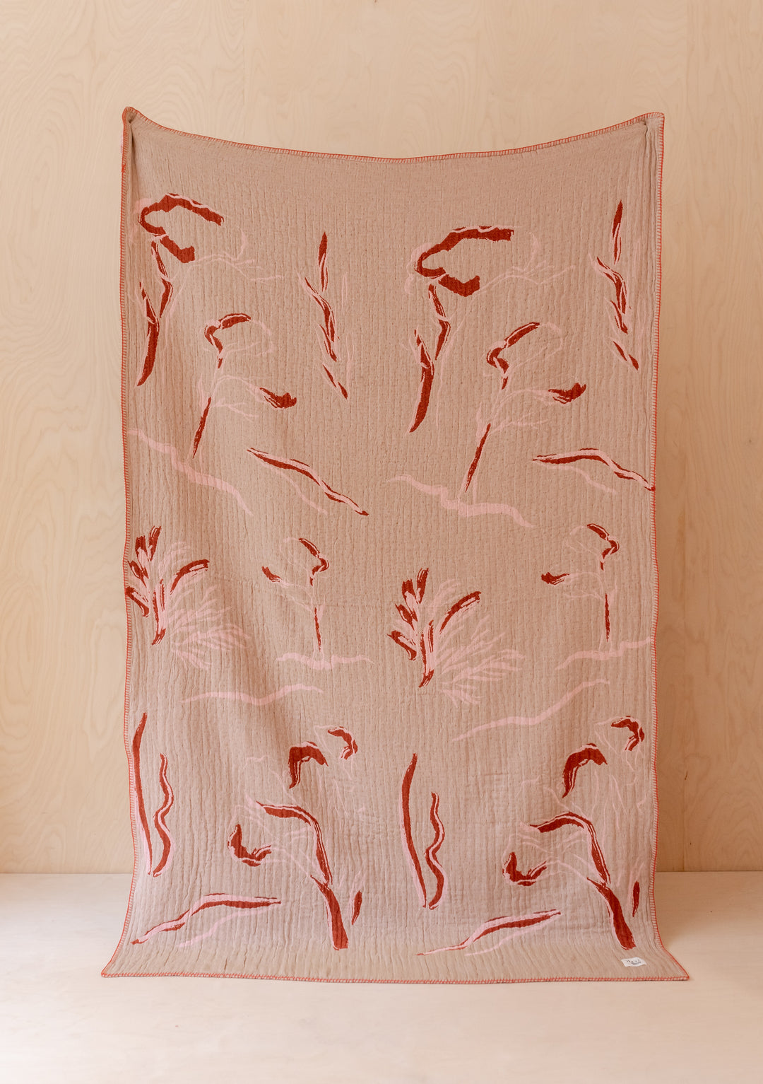 TBCo x Abisola Omole Reversible Wilderness Cotton Throw featuring tan base with red floral abstract pattern displayed flat