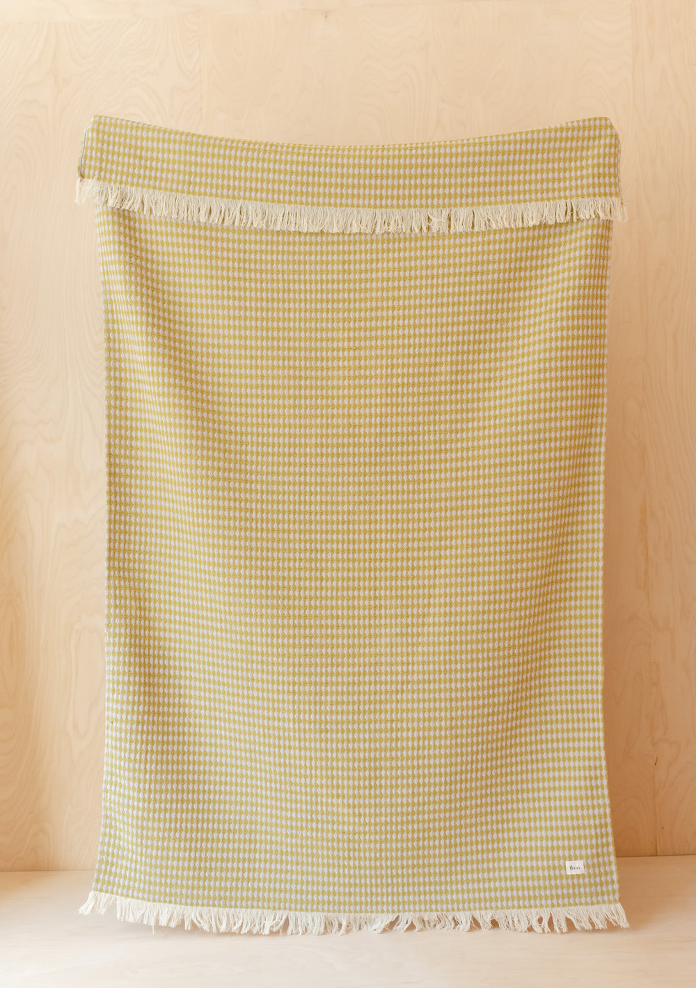 TBCo Cotton Throw in Olive Argyle displayed flat with fringed edges, showing textured geometric pattern against wooden background