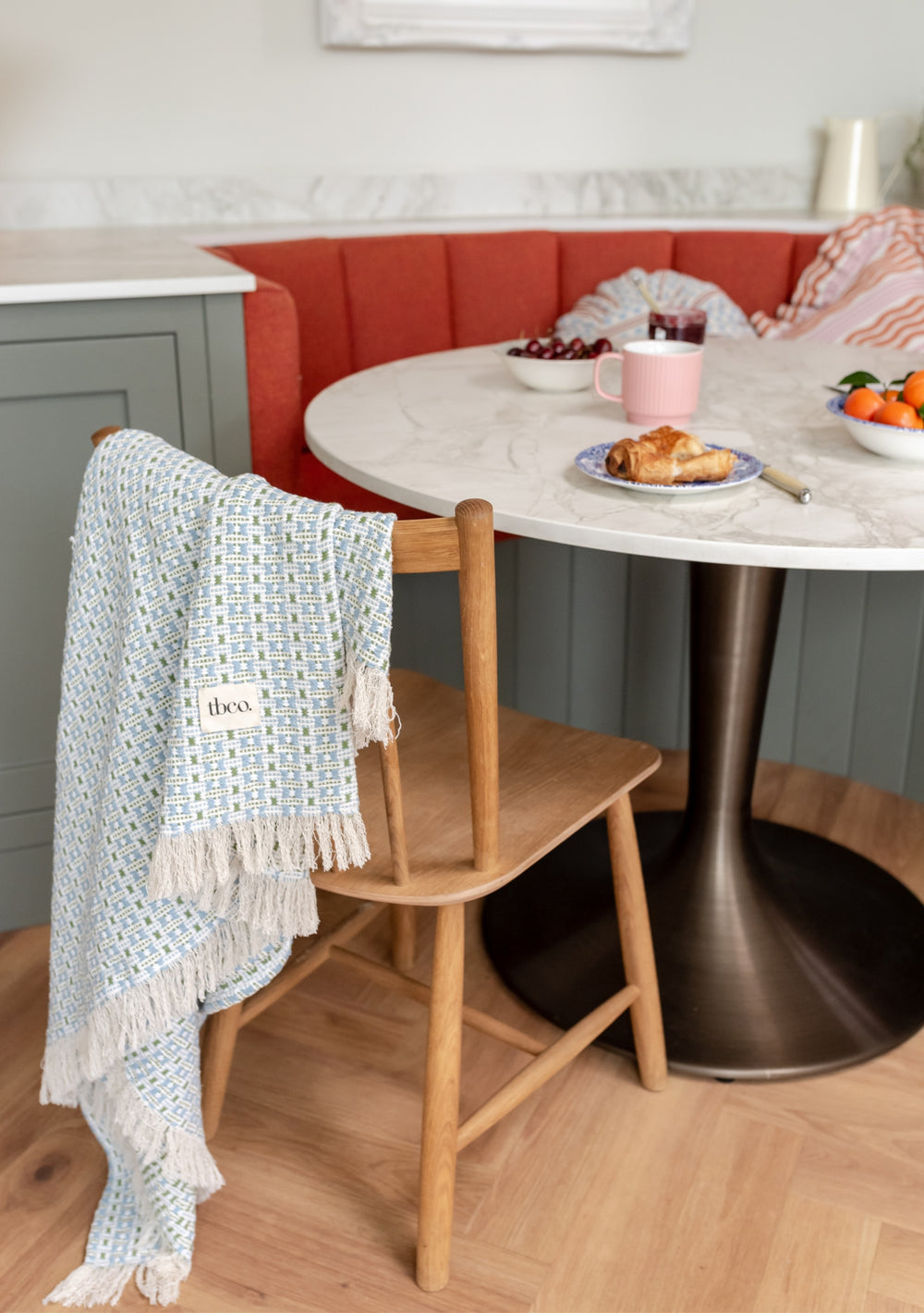 TBCo Cotton Throw in Green Geometric draped over wooden chair at marble dining table, showcasing woven jacquard pattern