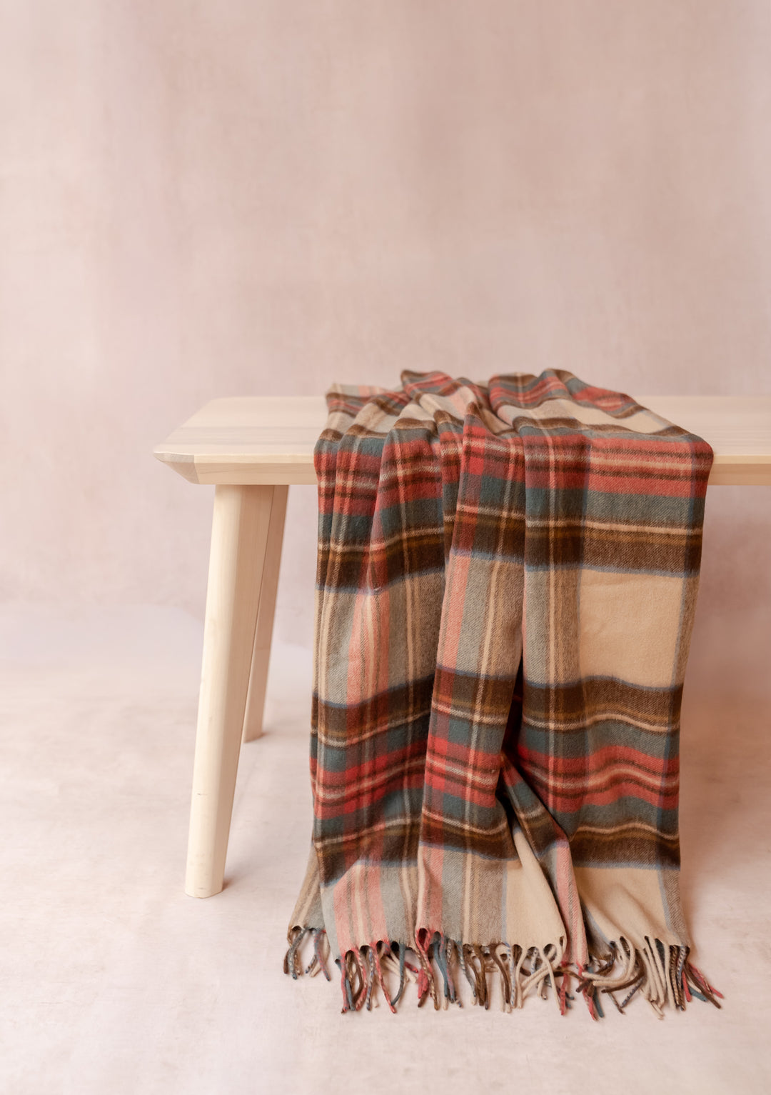 Cashmere Small Blanket in Stewart Dress Antique Tartan by TBCo draped over a light wooden bench with soft fringe detail