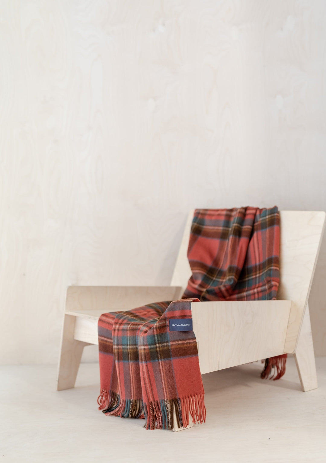 TBCo Stewart Royal Antique Tartan lambswool small blanket draped over modern wooden chair showing plaid pattern and fringe