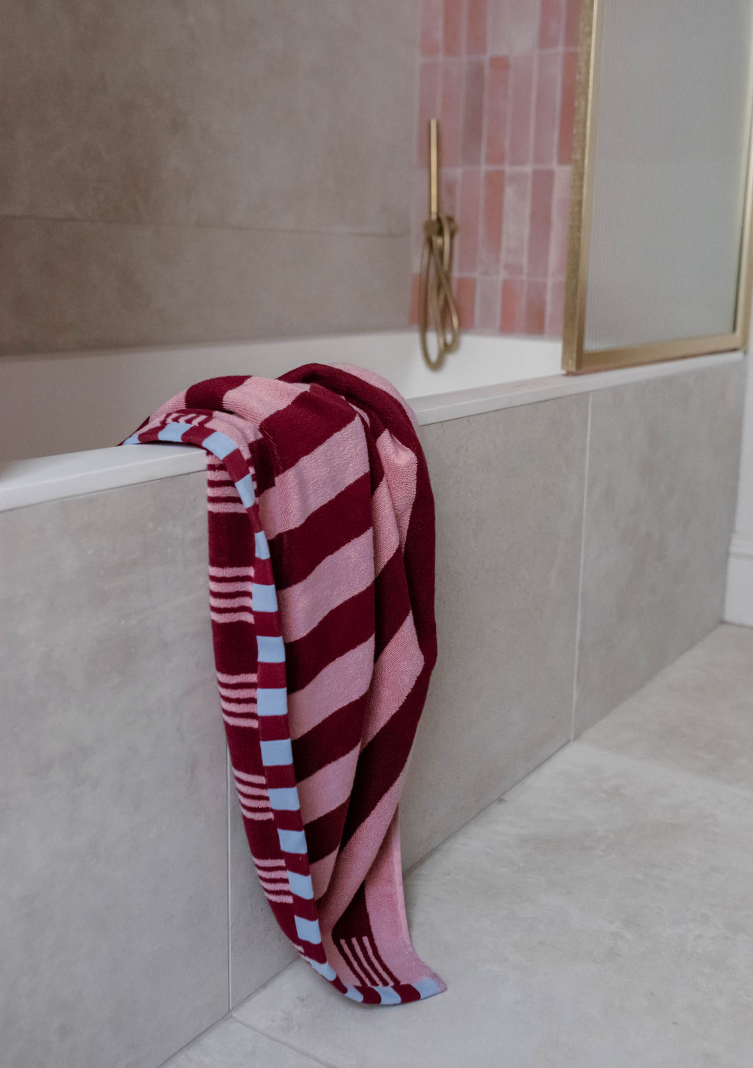 Soft TBCo Terry Cotton Towels in Burgundy Stripe casually draped over bathtub edge beside brass shower fixture