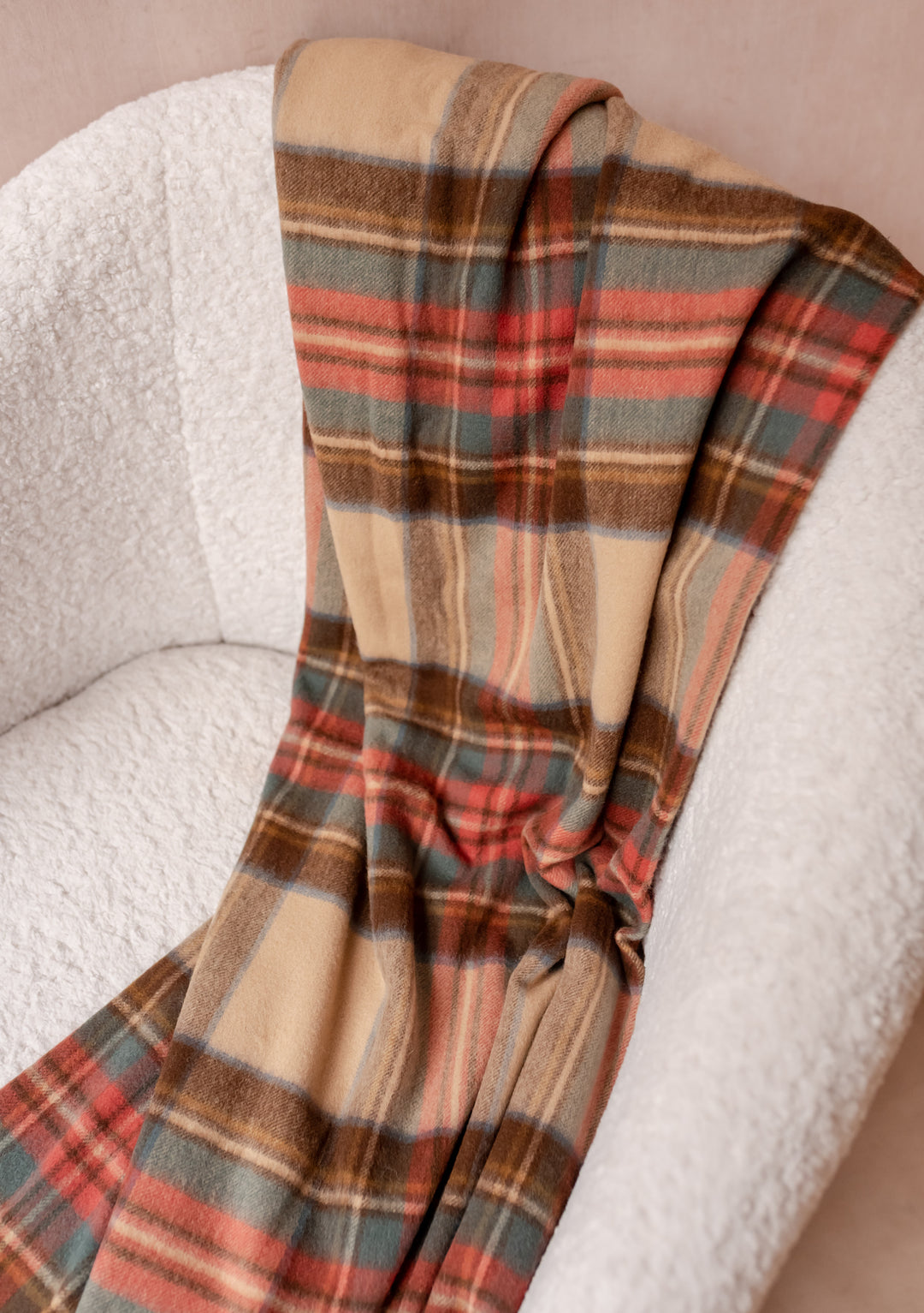 Cashmere Blanket in Stewart Dress Antique Tartan by TBCo draped over a textured cream boucle armchair with soft folds