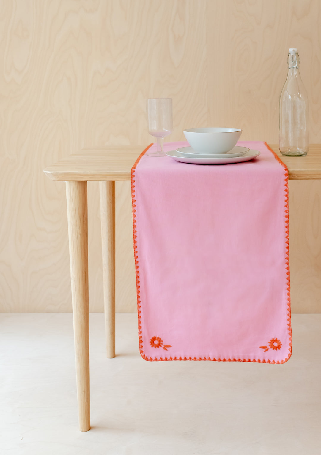 TBCo Cotton & Linen Table Runner in pink with orange embroidered edge and floral details, styled on wooden table with dinnerware