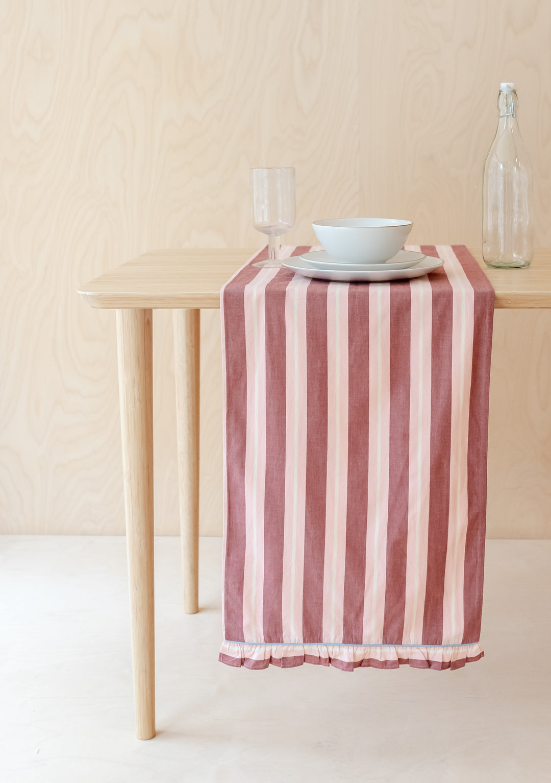 TBCo Cotton Runner in Red Stripe displayed on wooden table with frilled edges and pink stripes, styled with tableware