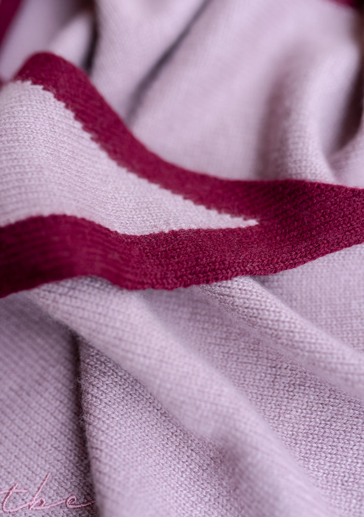 Close-up detail of TBCo Merino Triangle Scarf in lilac with burgundy border, showing soft knitted wool texture and brand embroidery