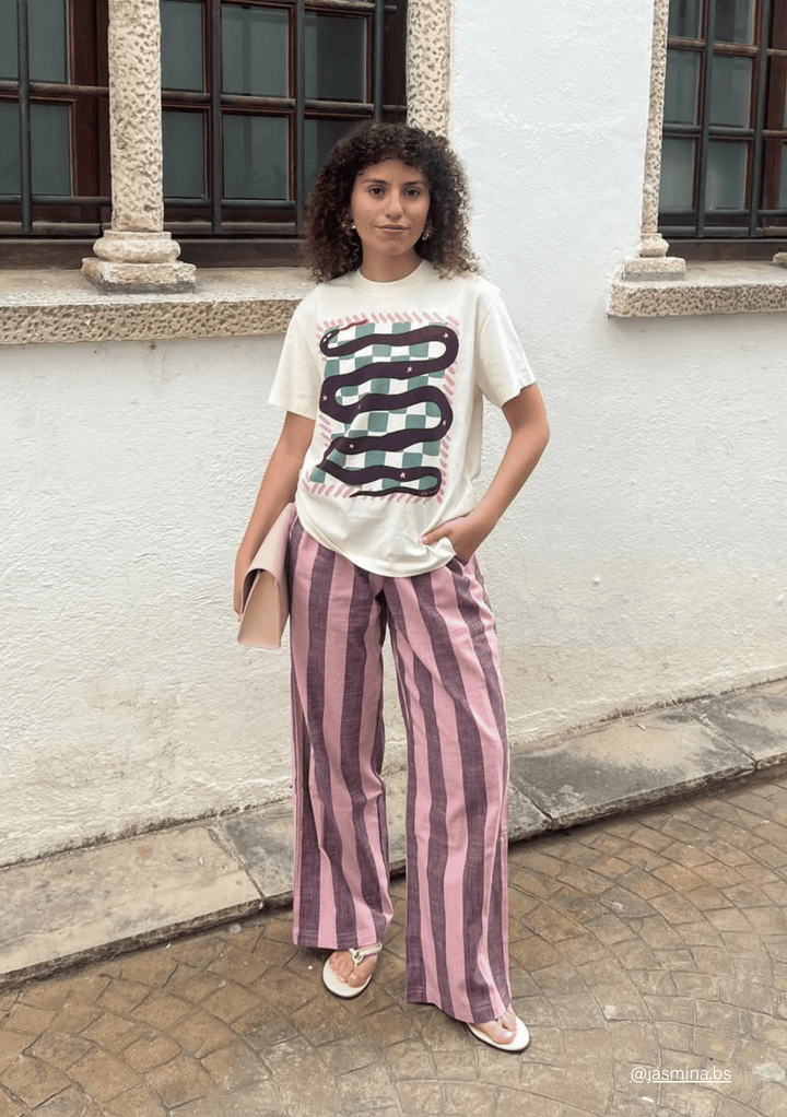 Woman wearing a TBCo Cotton graphic snake t-shirt and striped Pink & Burgundy Cotton trousers standing in front of a building.