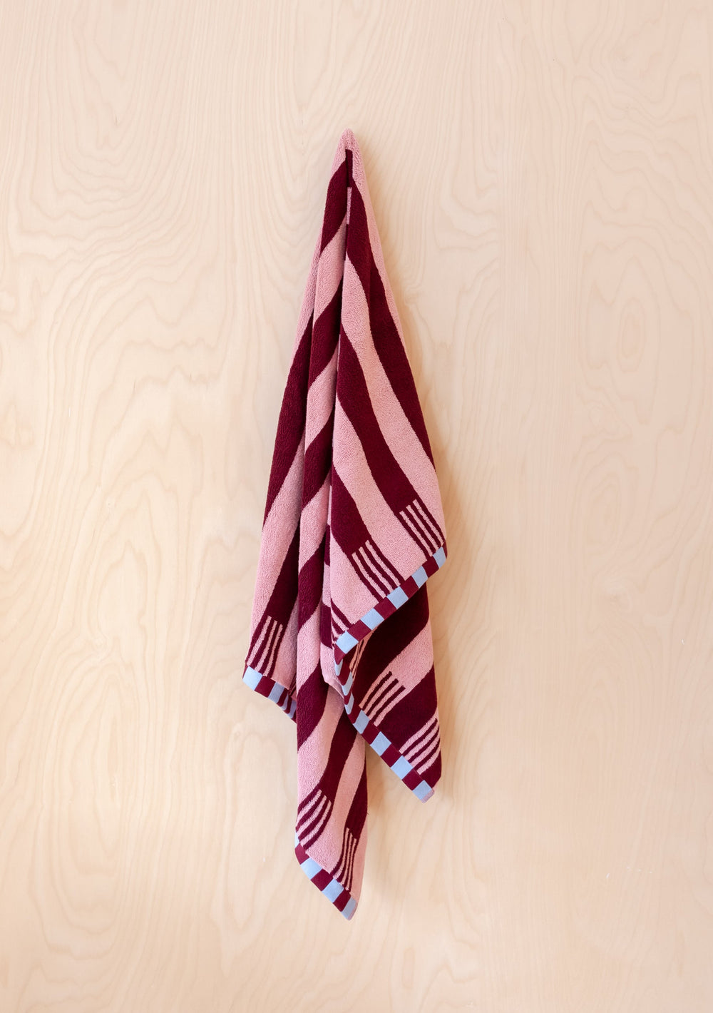 Luxury TBCo Cotton Towels in Pink Stripe with burgundy pattern and blue checkerboard trim hanging elegantly against cream wall